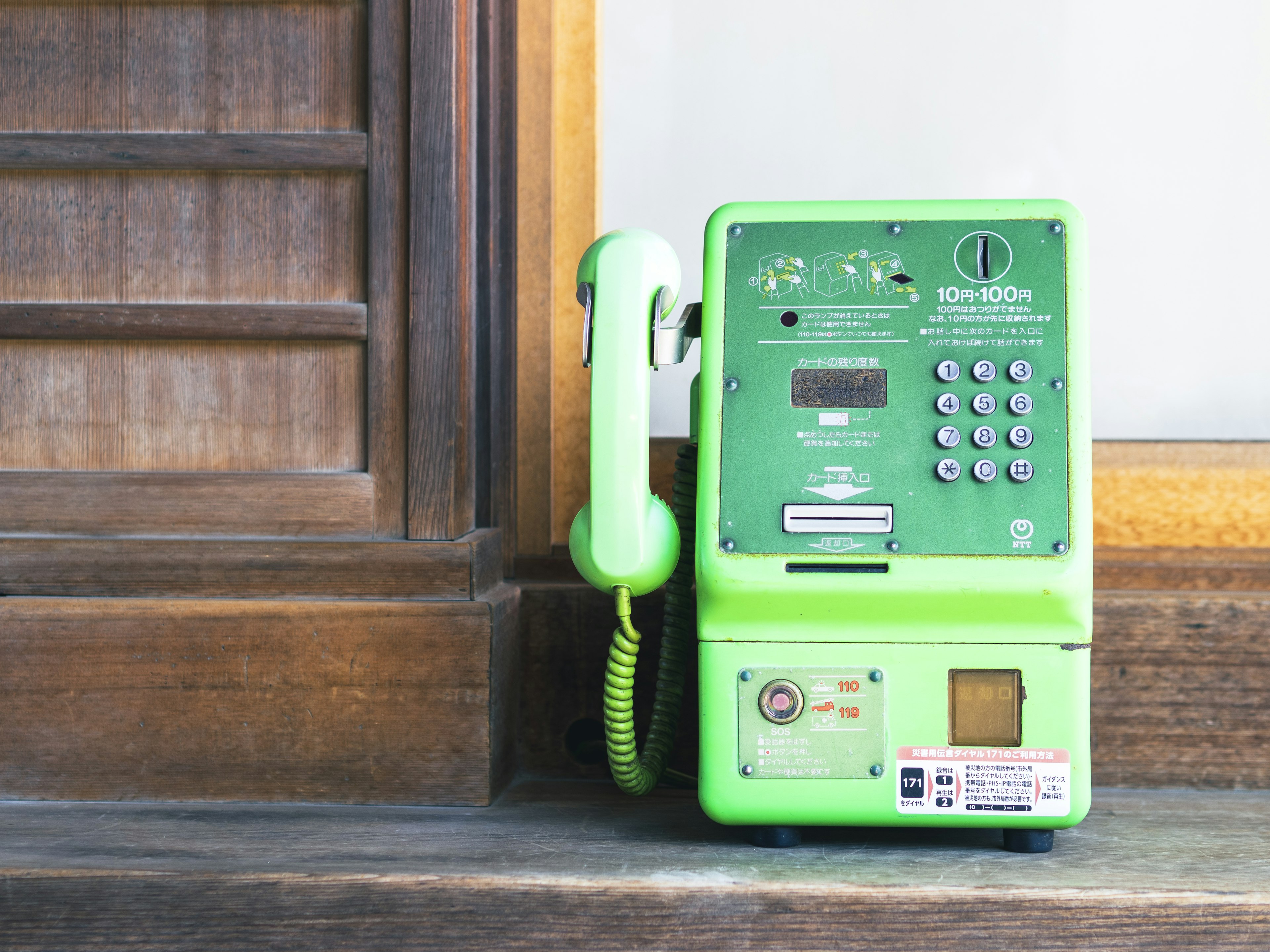 Teléfono público verde al lado de una pared de madera