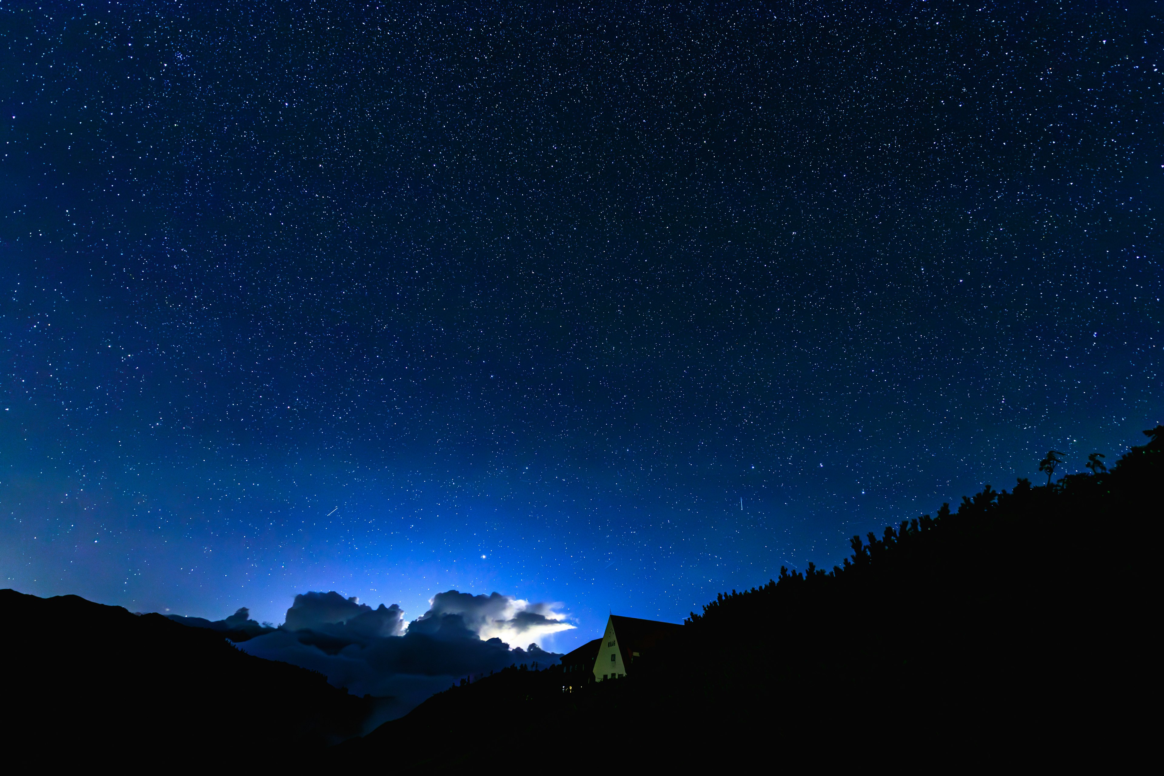 Ciel nocturne rempli d'étoiles avec des montagnes en silhouette au premier plan