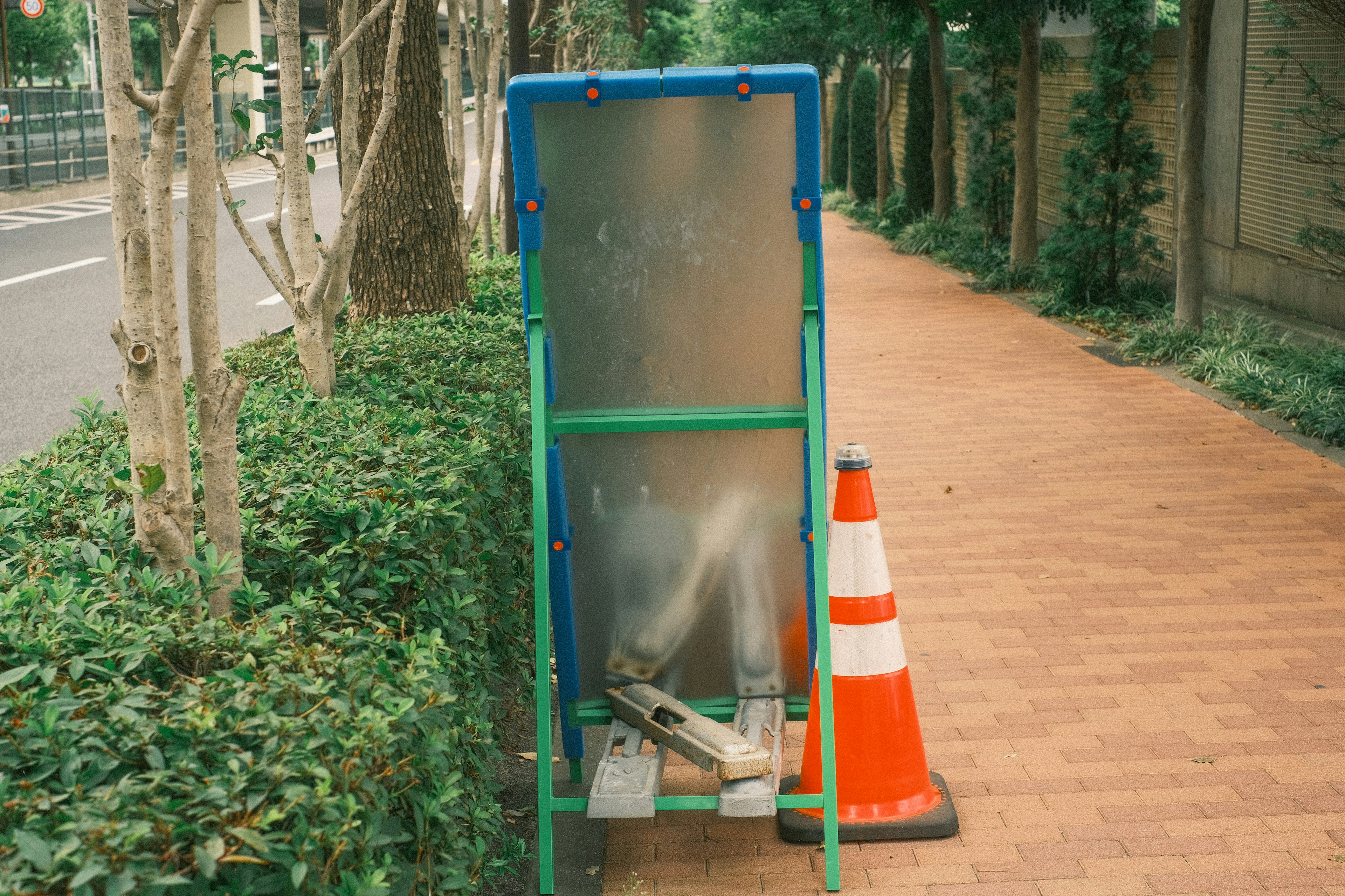 通りに立てられた緑色の看板とオレンジ色のコーンがある歩道の風景