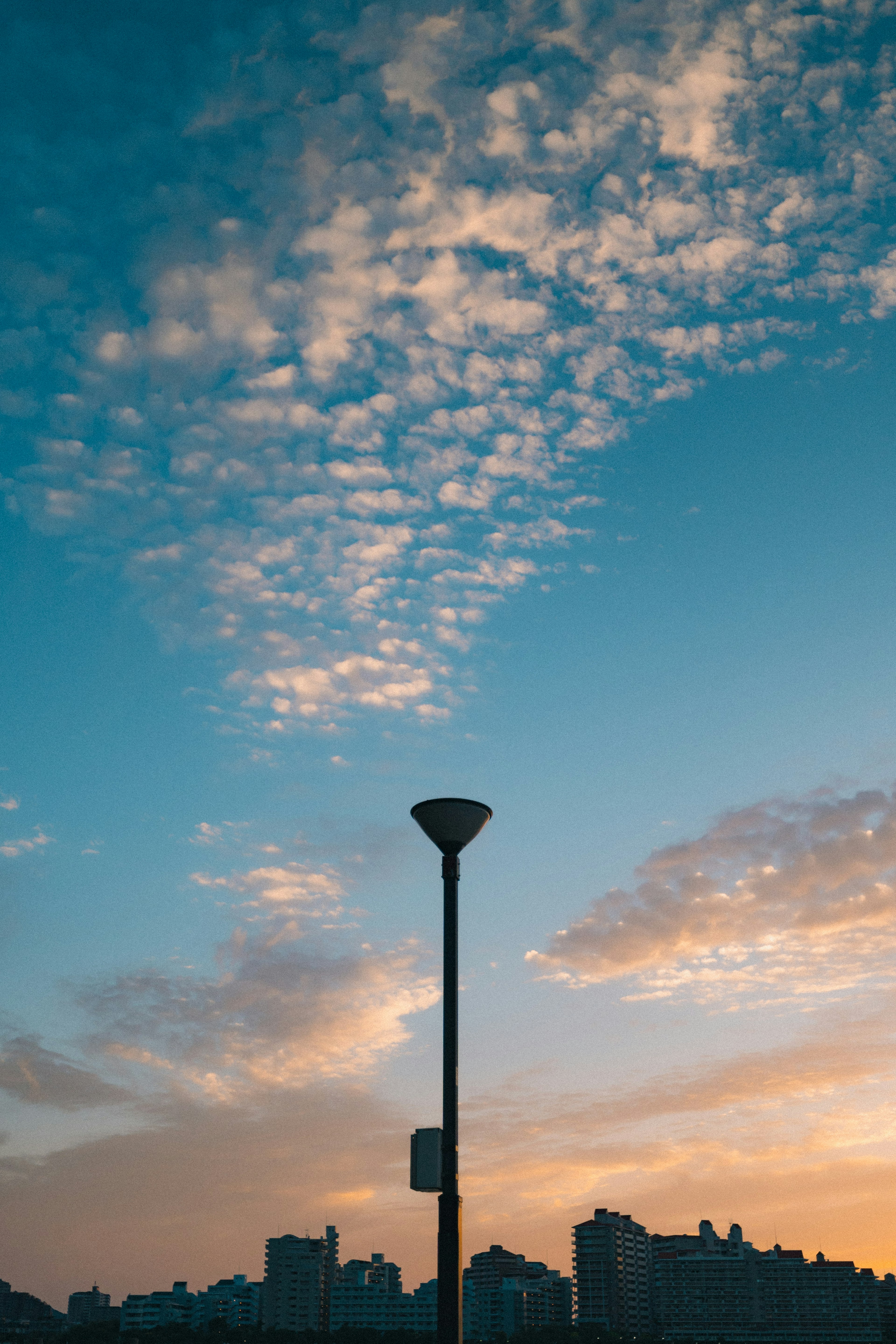 Silhouette einer Straßenlaterne vor einem blauen Himmel mit Wolken