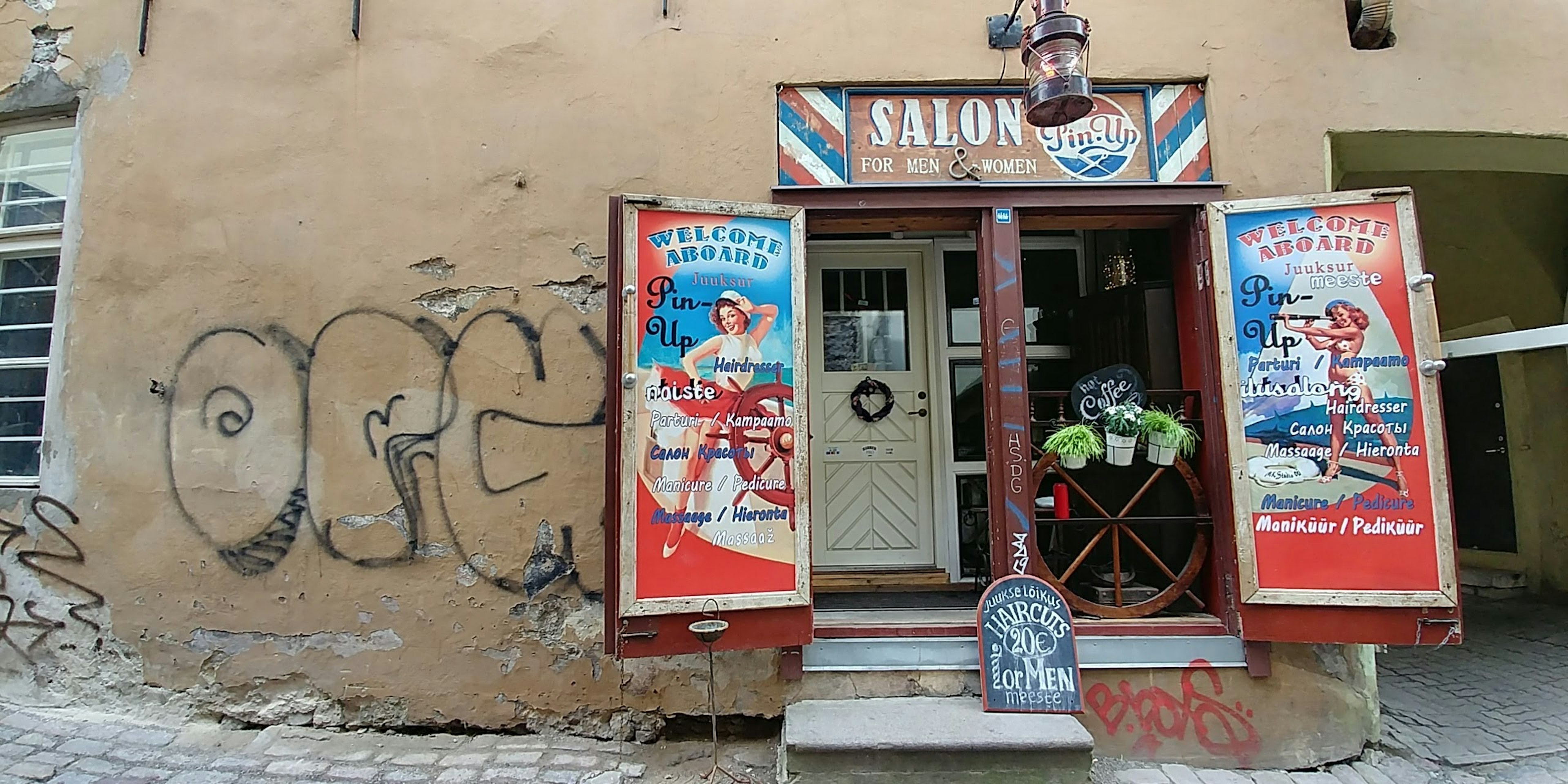 Außenansicht eines Friseursalons mit bunten Schildern und Türen, Graffiti an der Wand