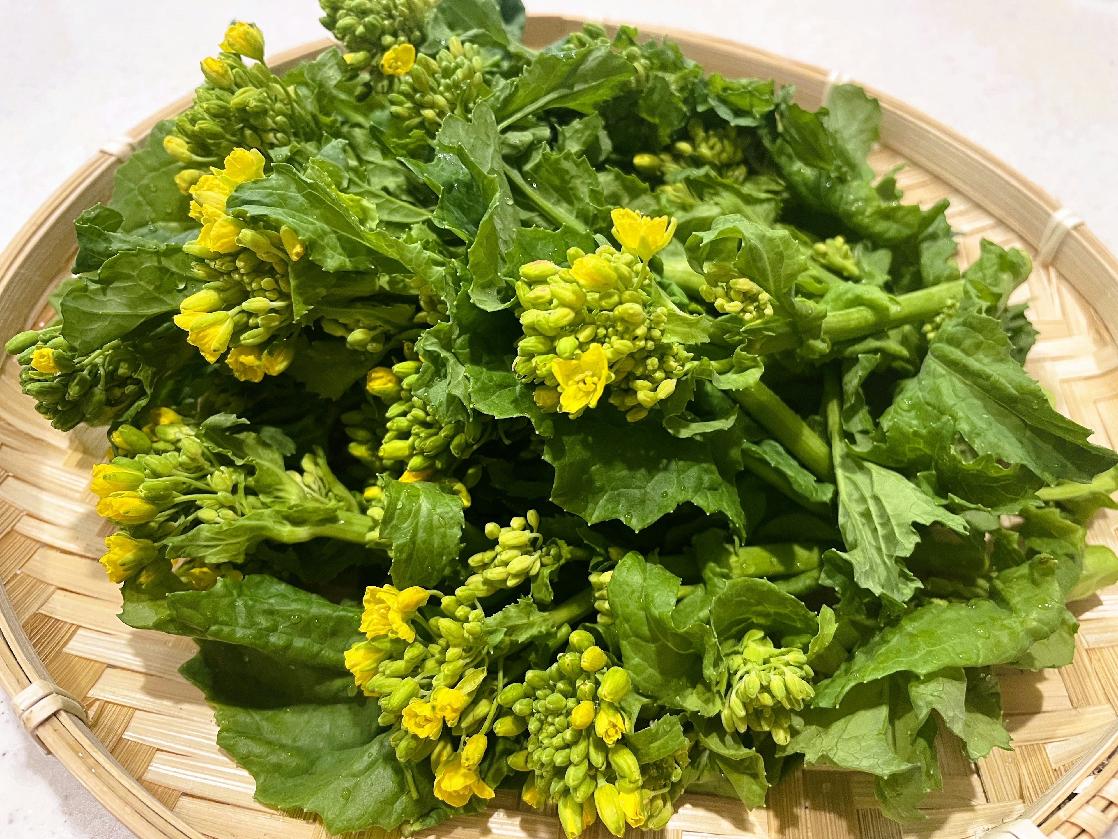 A bundle of green vegetables with yellow flowers arranged in a bamboo basket