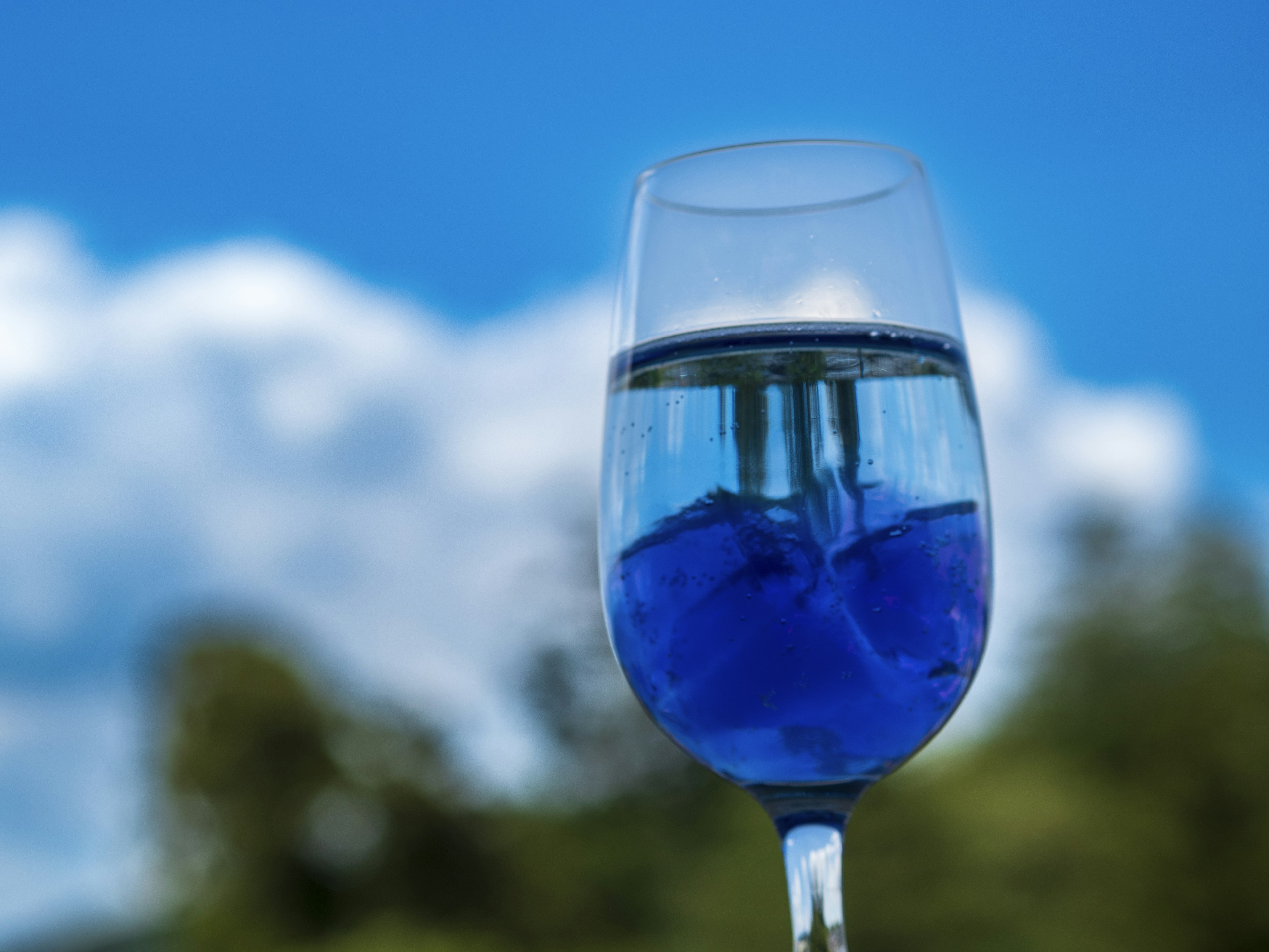 A clear glass with blue ice and a blue sky background