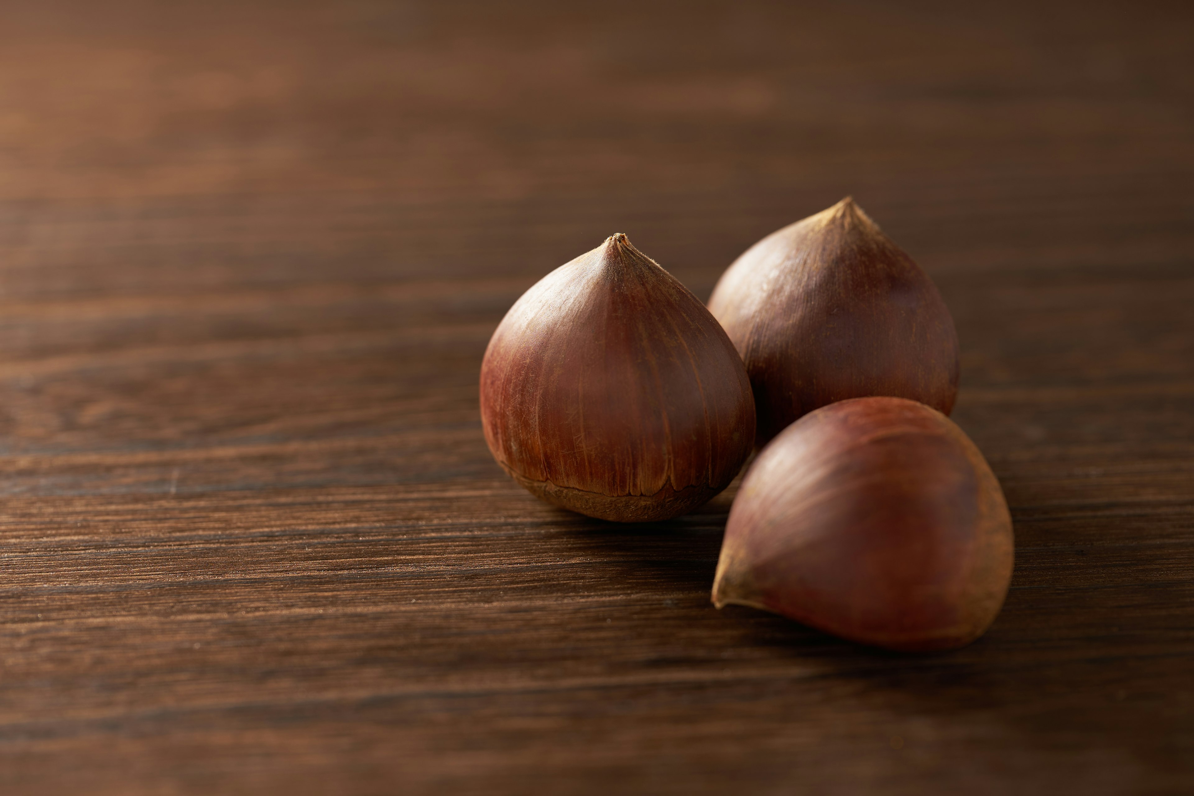 Three reddish-brown hazelnuts on a wooden table