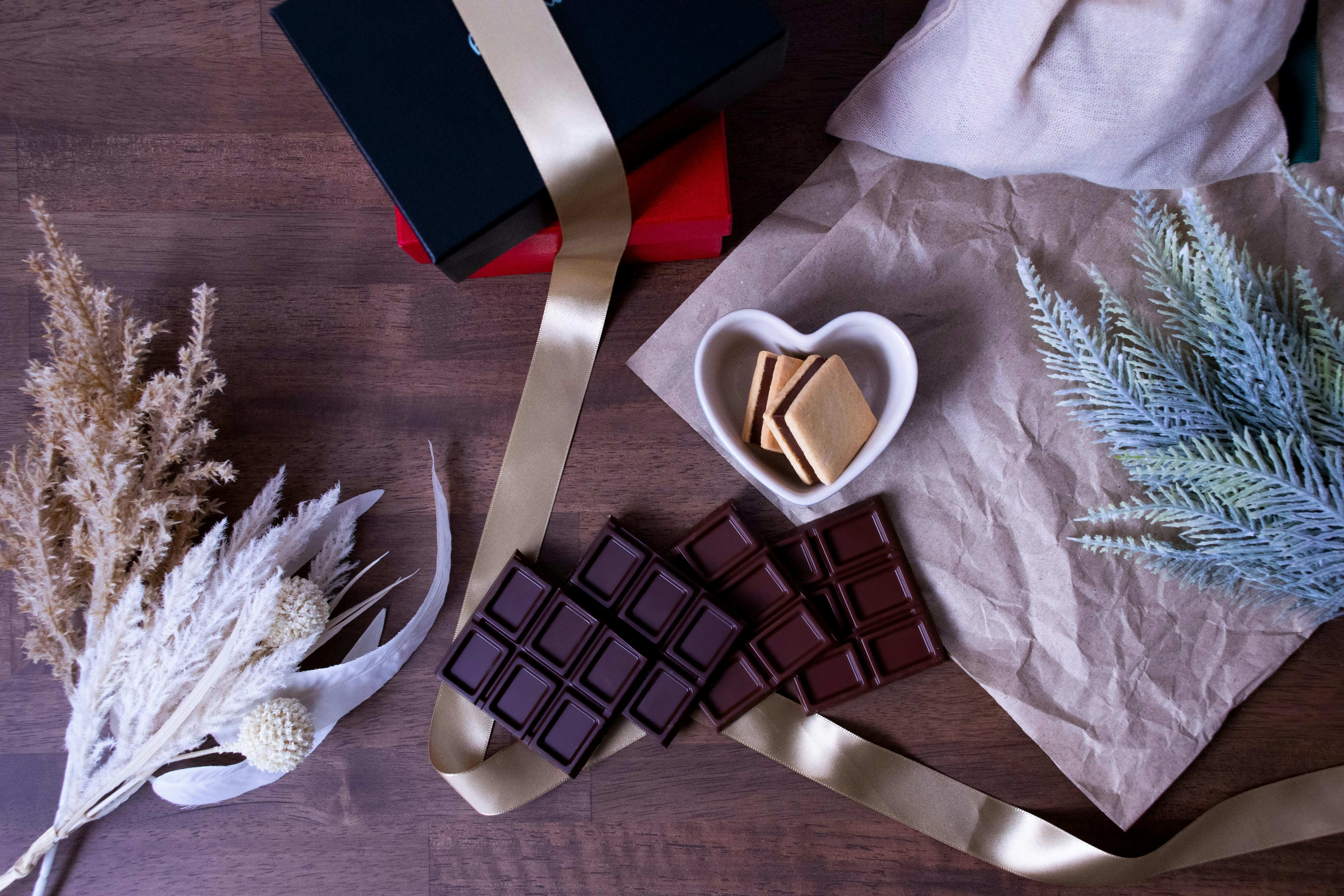 Dark chocolate pieces next to a heart-shaped dish with cookies on a textured surface