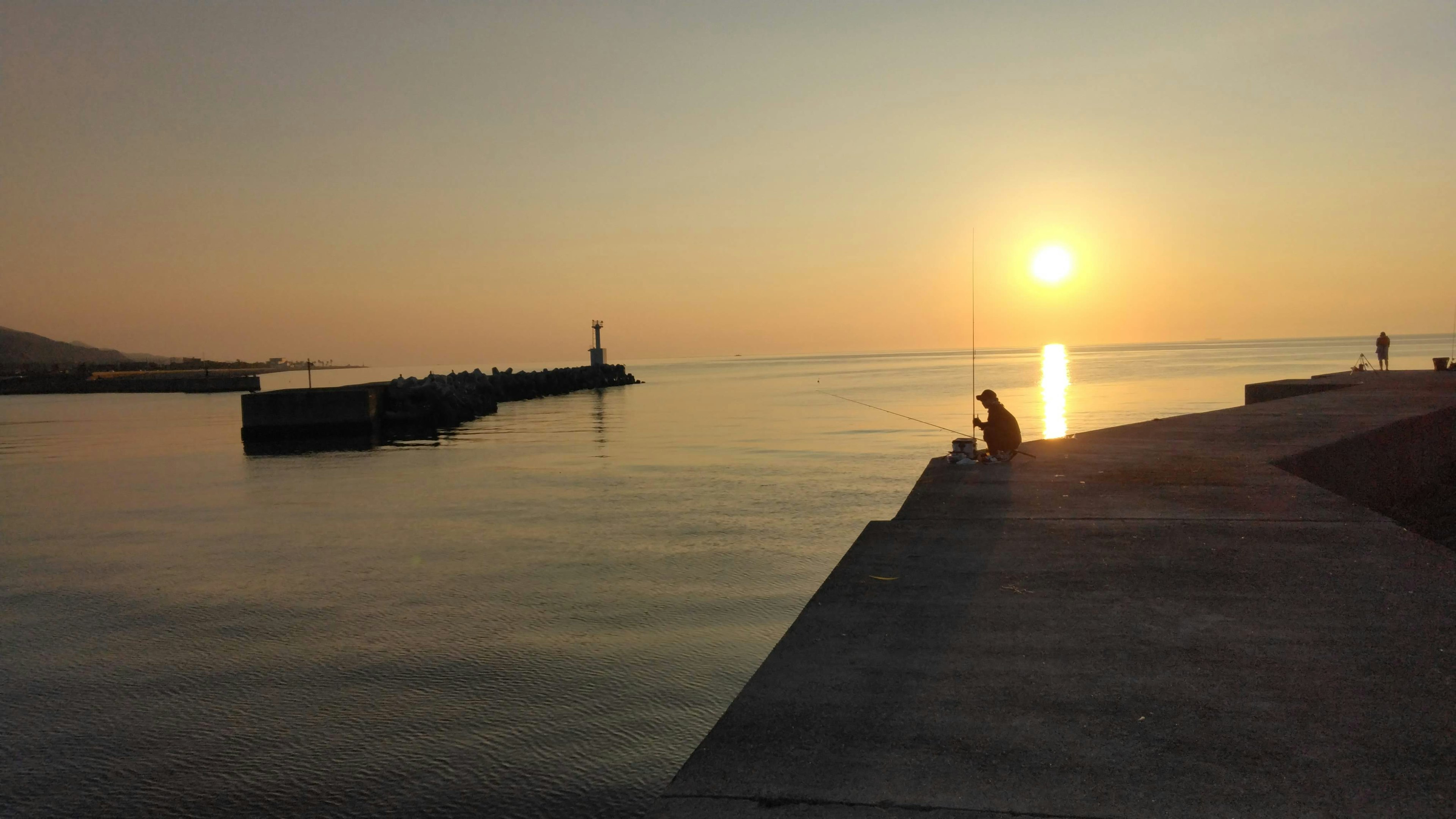 Eine Person sitzt am ruhigen Meer und schaut den Sonnenuntergang an