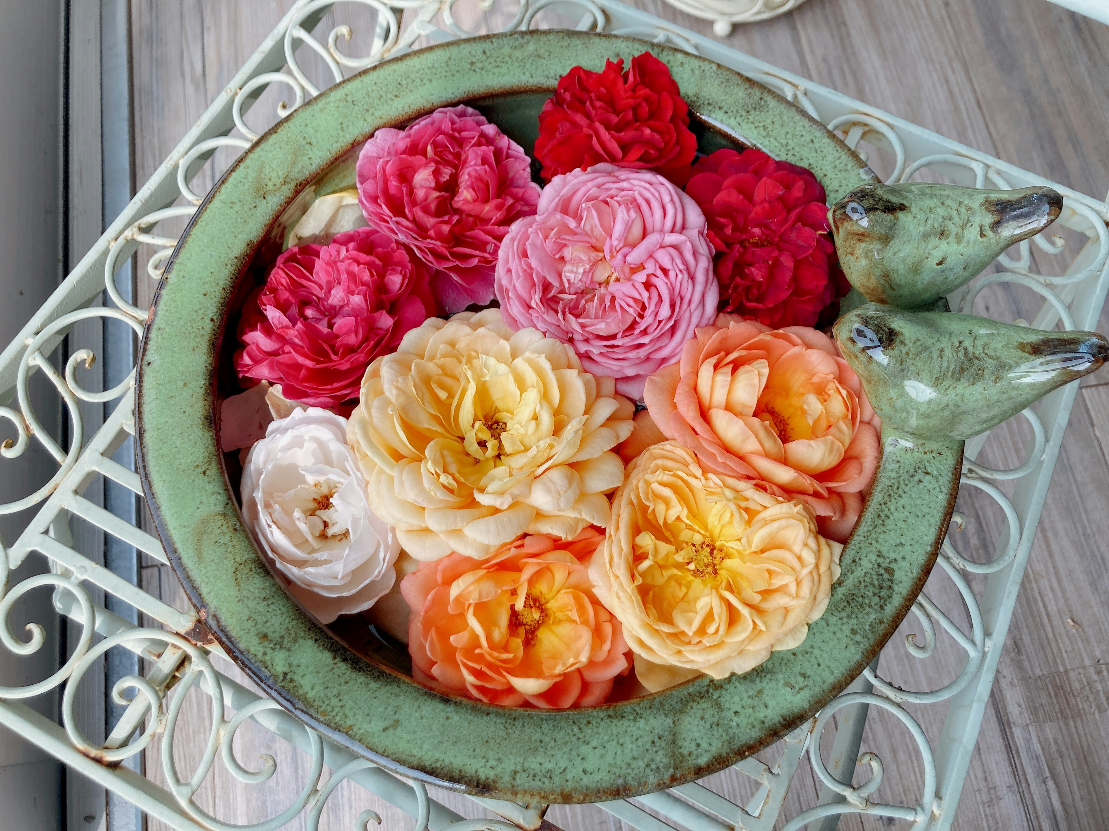 Colorful flowers arranged in a green bowl with decorative birds