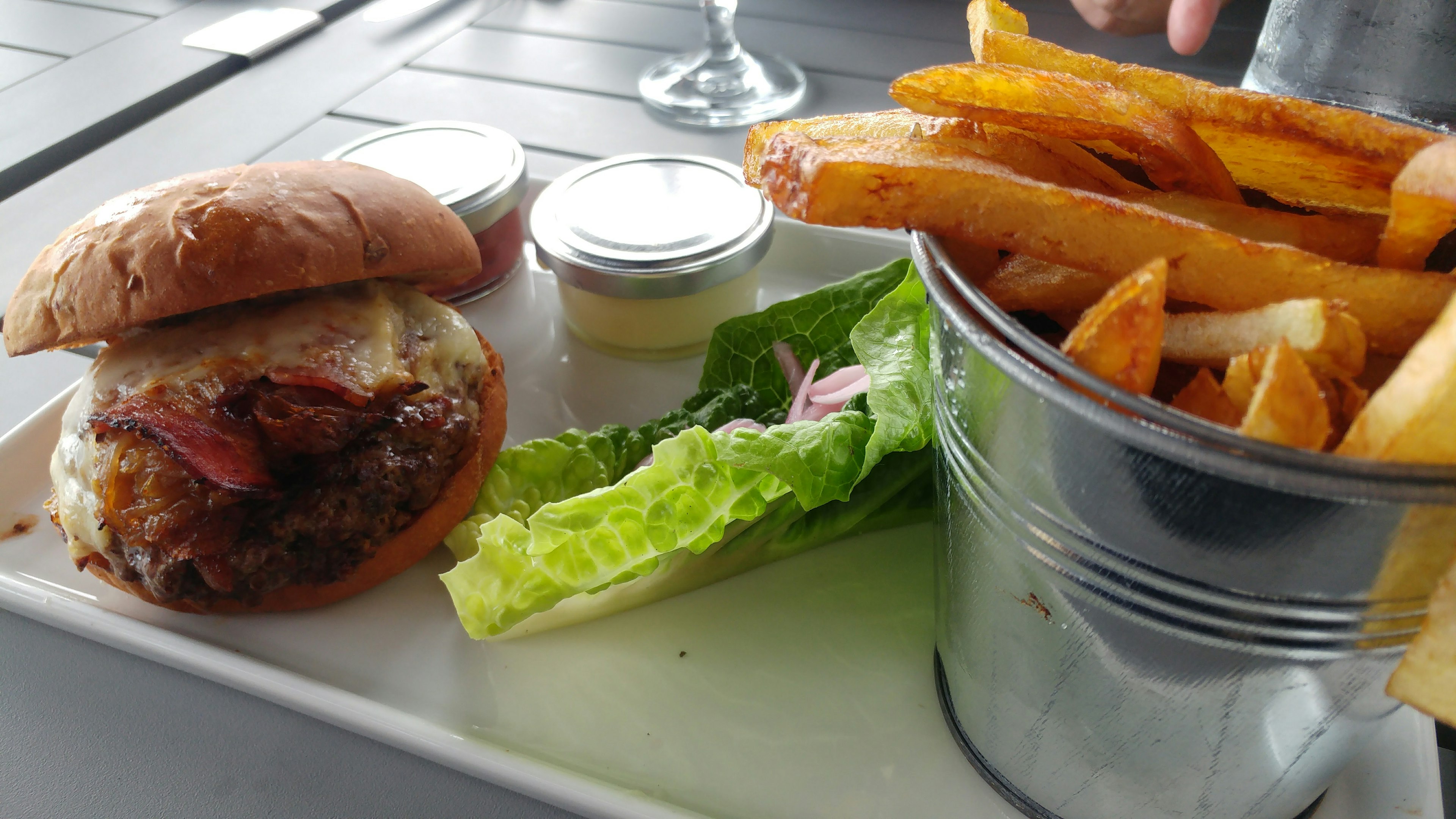 Un piatto con un hamburger con guarnizione lattuga e due salse affiancato da un secchio di patatine fritte