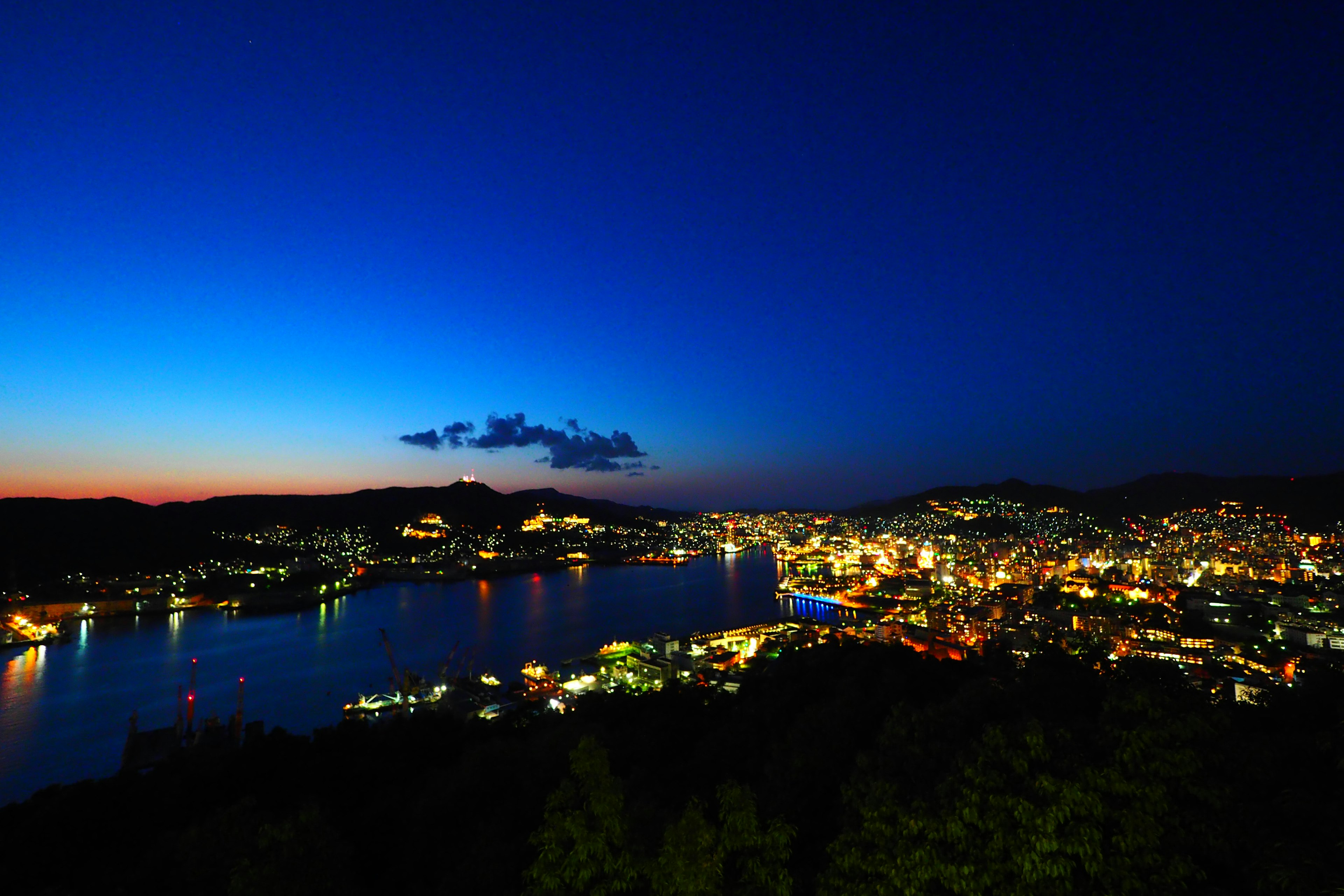 Panoramablick auf eine Hafenstadt bei Nacht mit blauem Himmel und beleuchteten Gebäuden