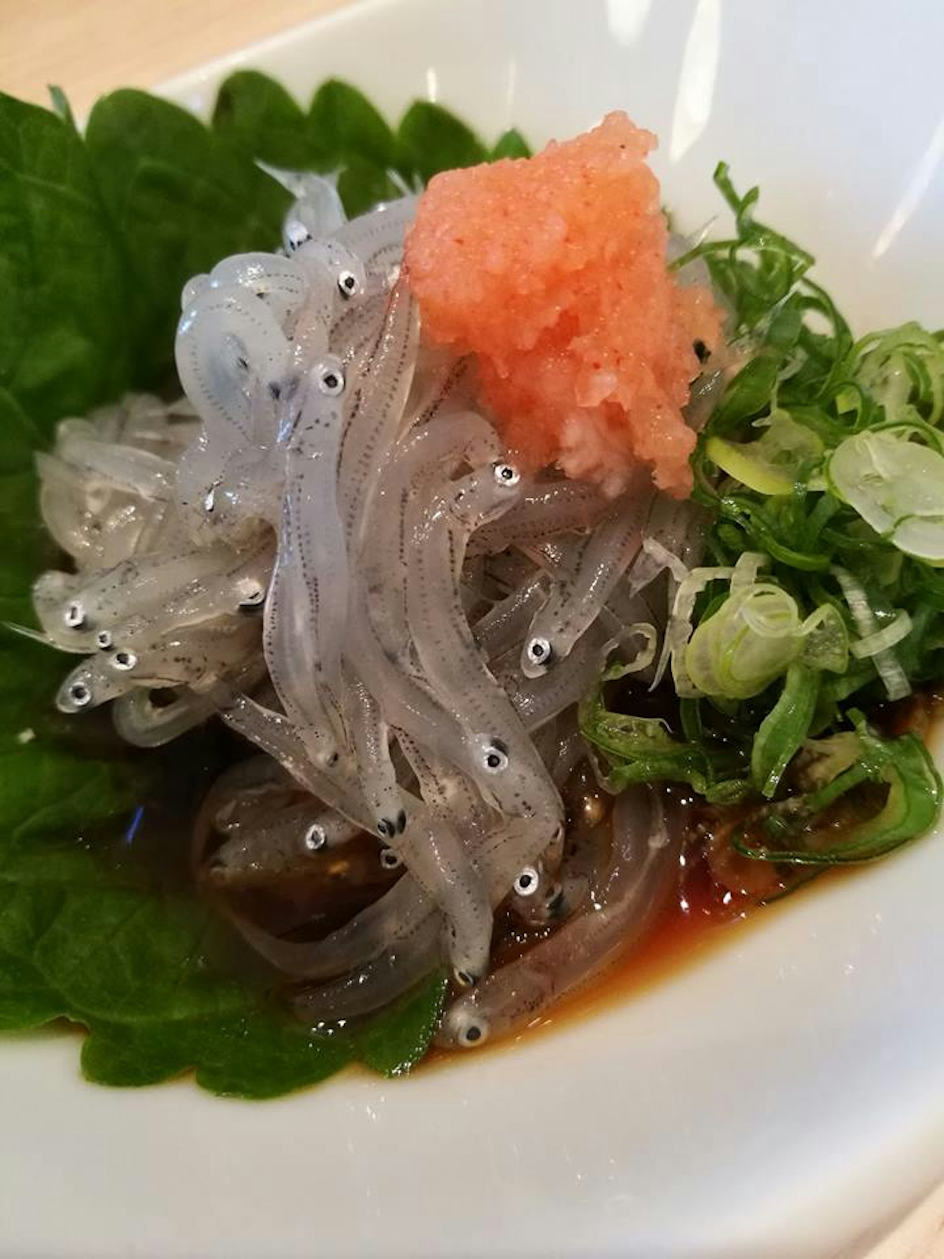 Dish featuring transparent small fish with green onions and a dollop of pink paste