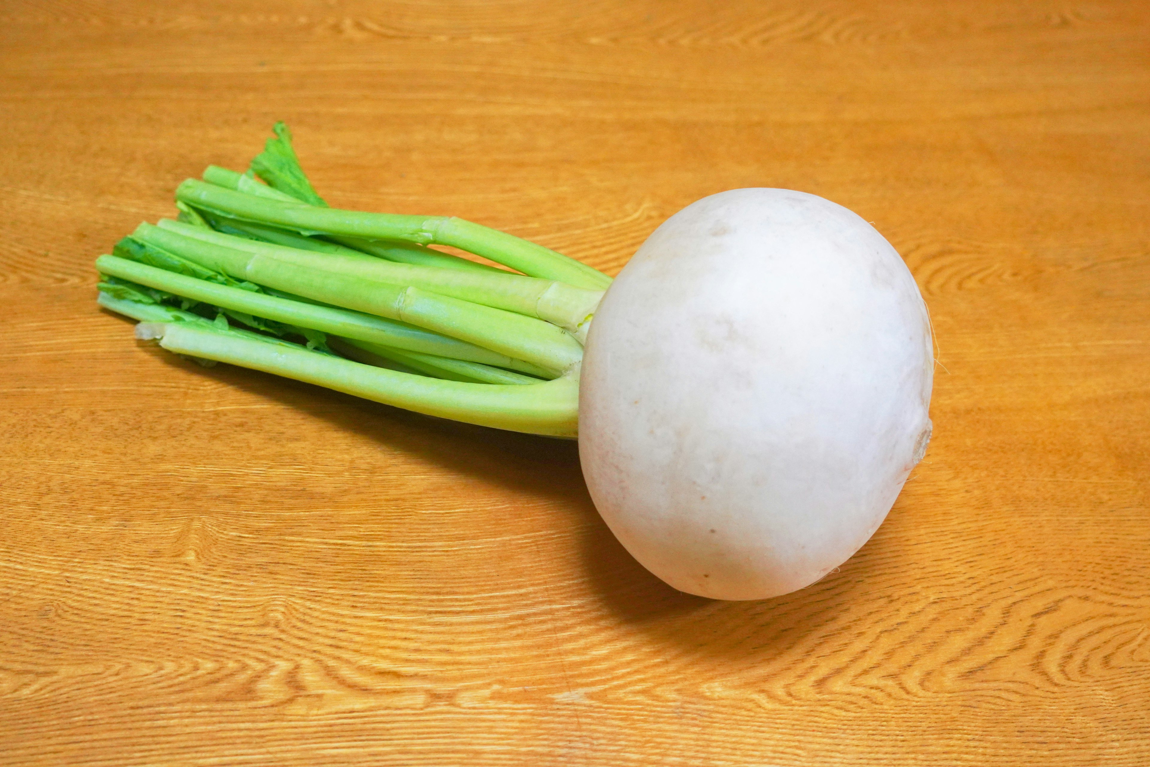 Un daikon bianco con foglie verdi su una superficie di legno