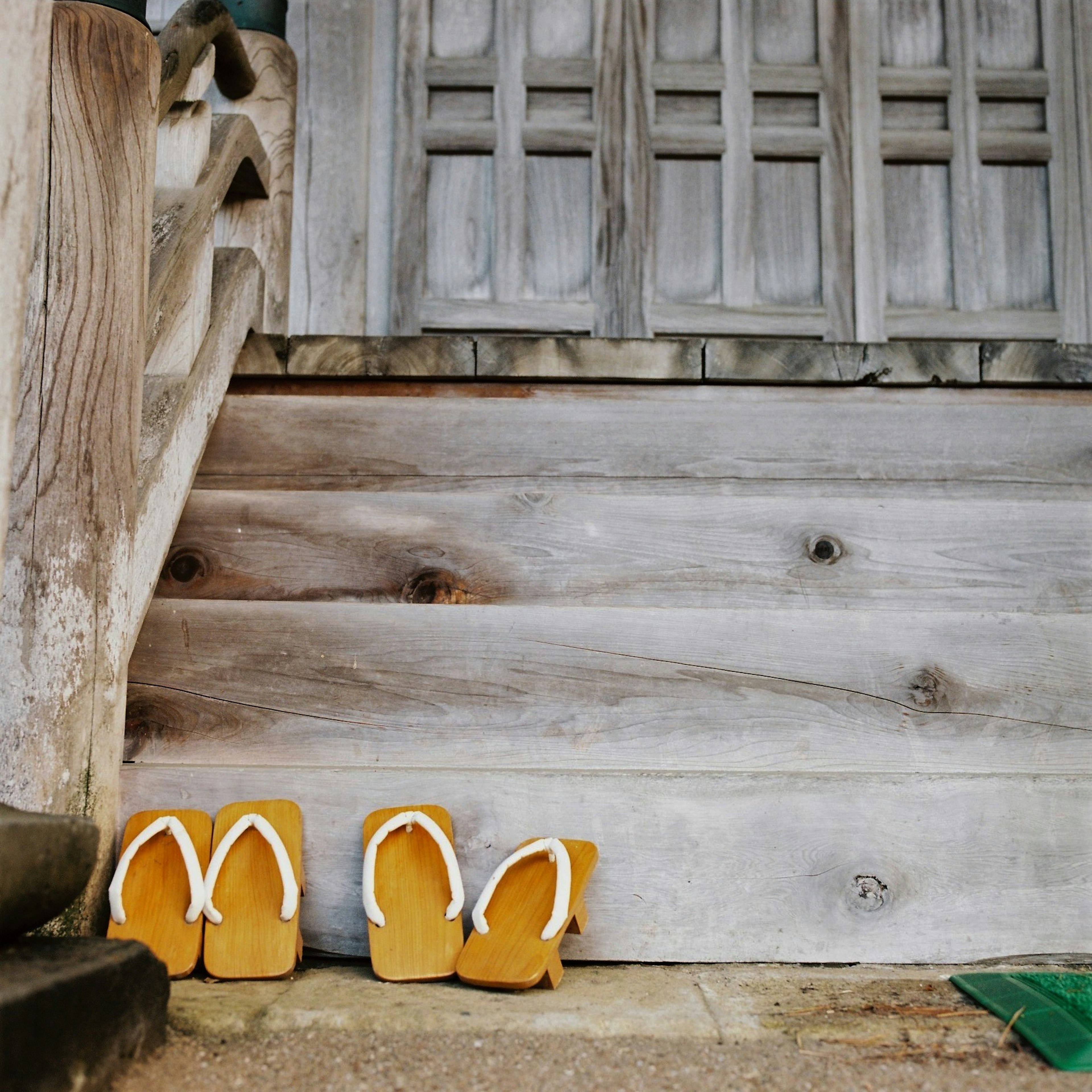 Sandals kayu tradisional diletakkan di depan tangga kayu dan dinding kayu tua