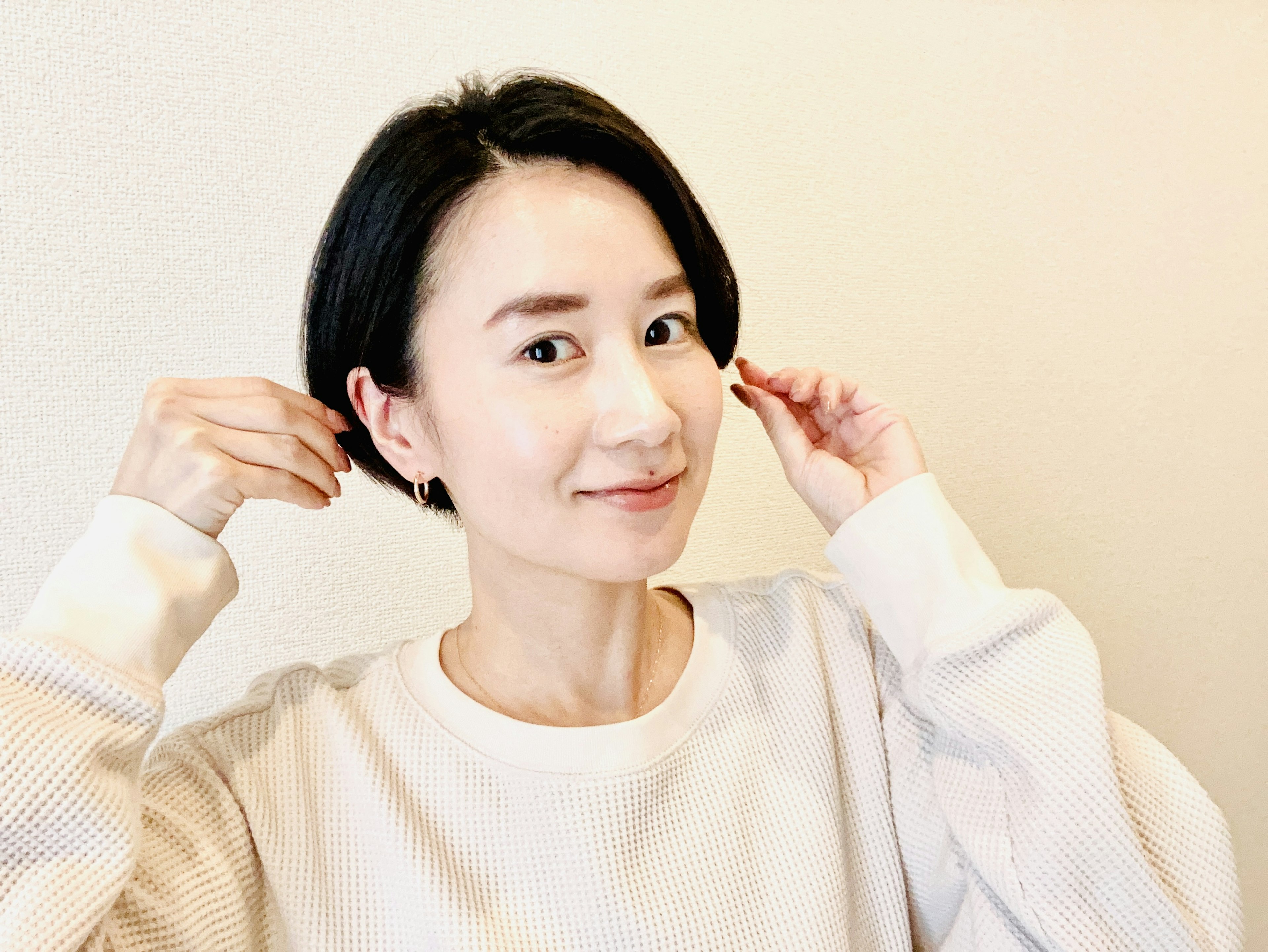 A woman smiling in a white sweater with short black hair