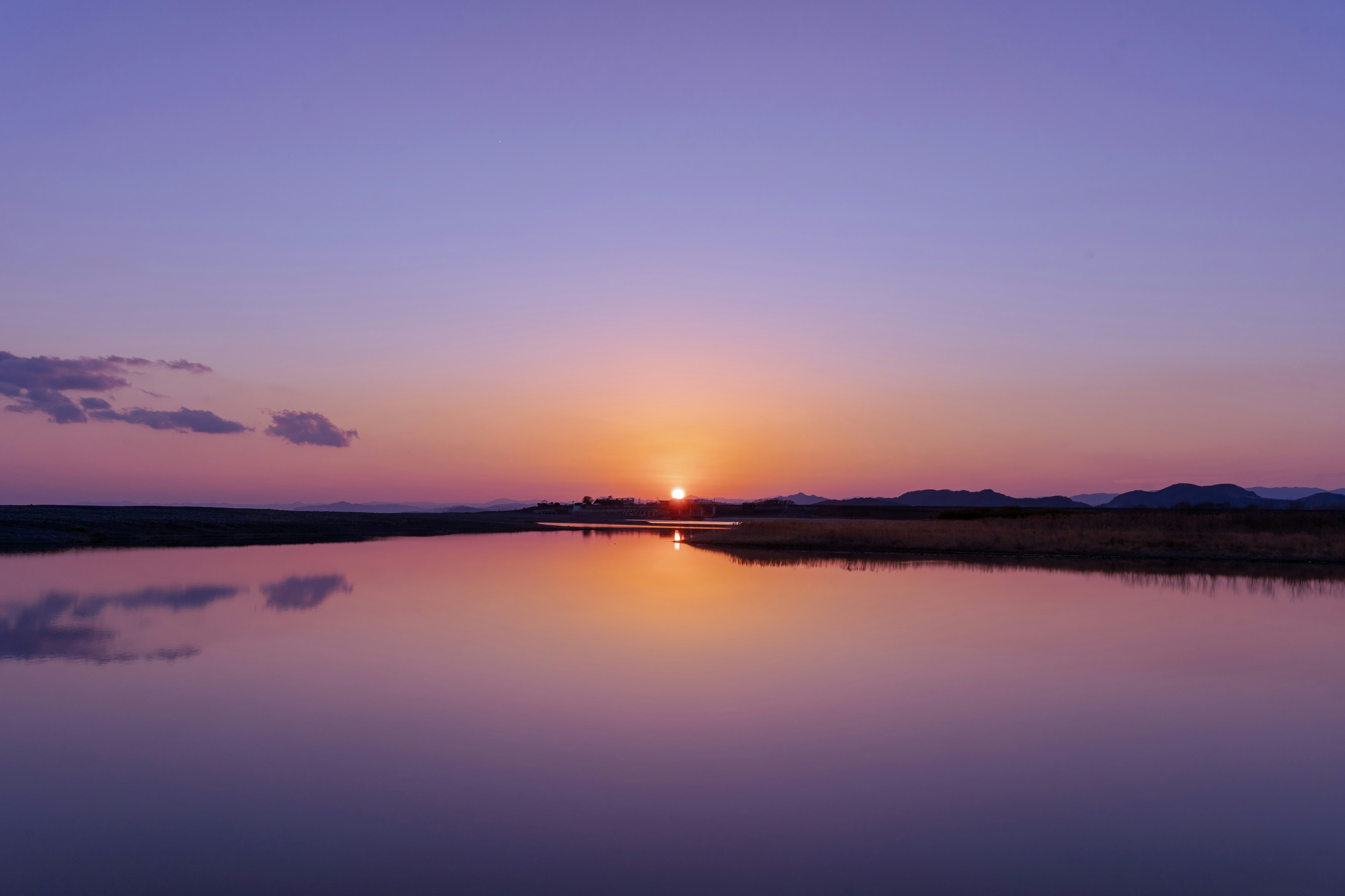 静かな水面に映る夕日と紫色の空