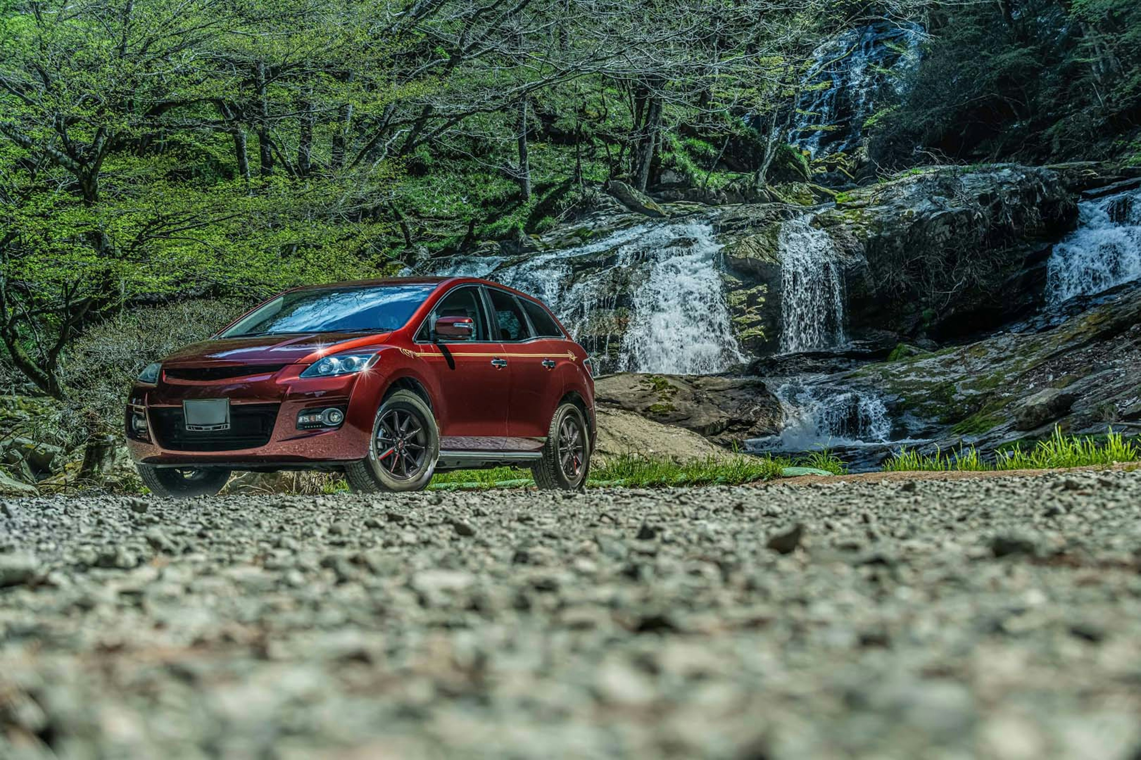 SUV rosso parcheggiato vicino a una cascata in un ambiente naturale