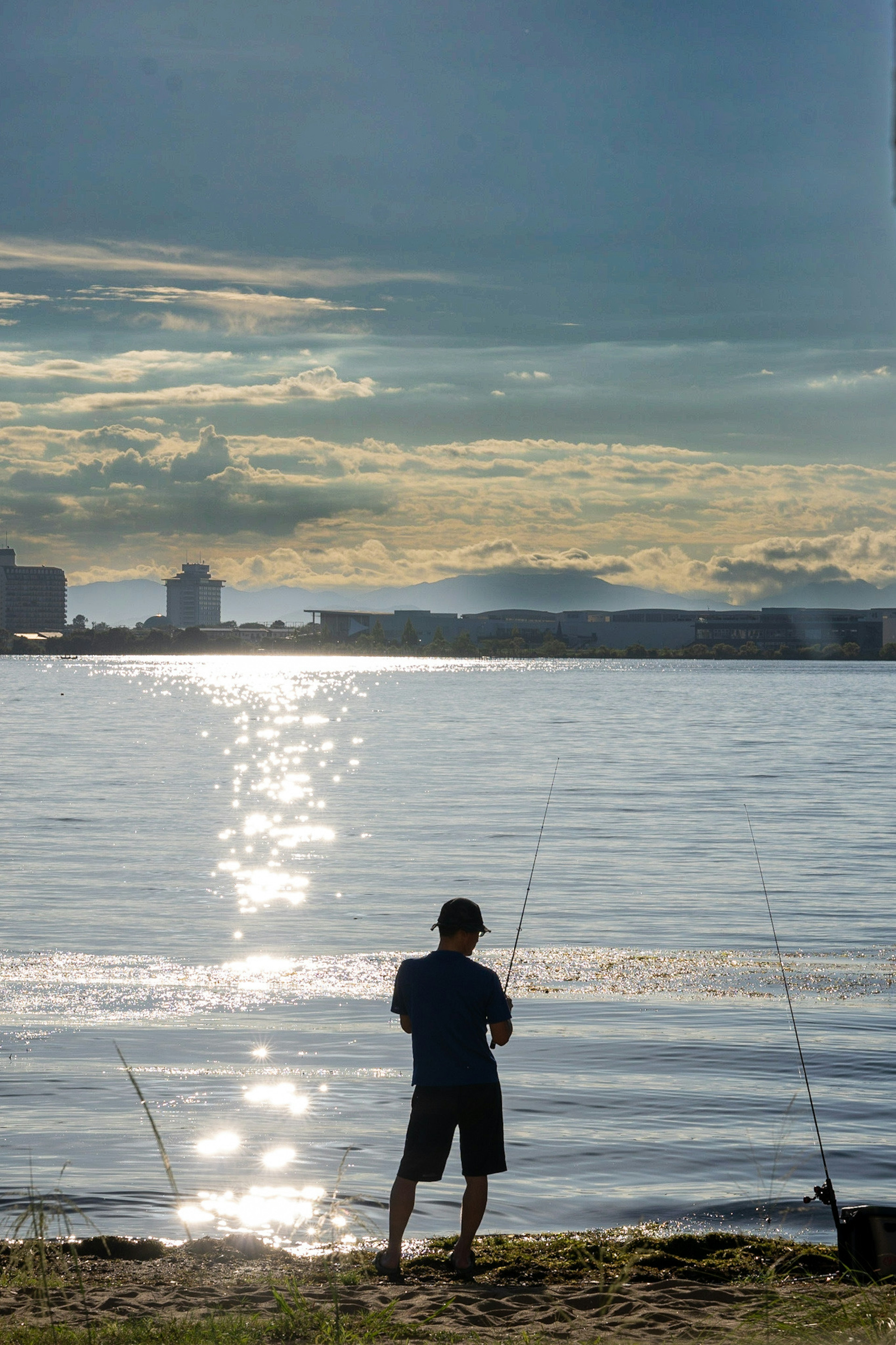 Silhouette seorang anak yang sedang memancing di tepi air dengan pantulan matahari terbenam