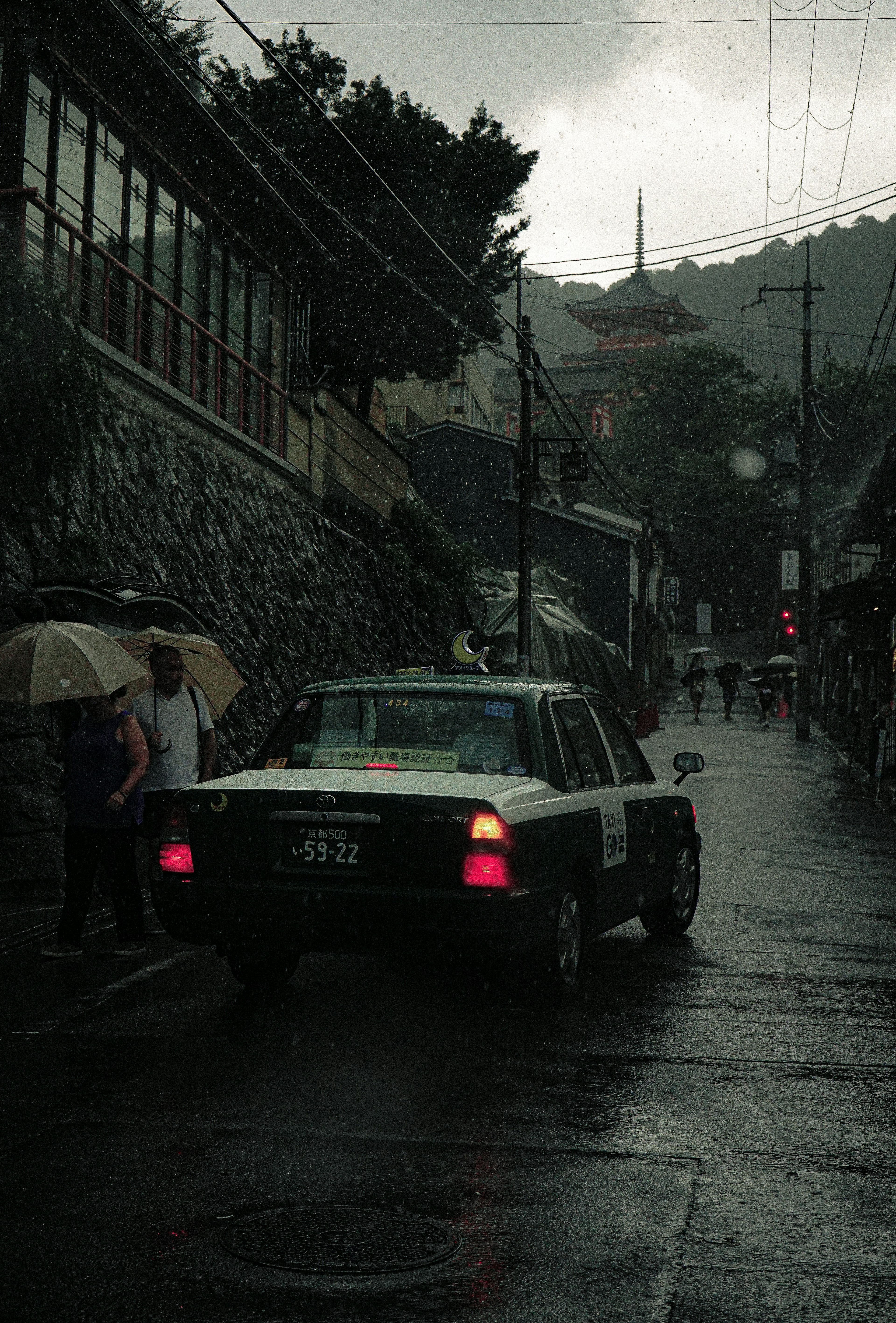 雨の降る街角に停車するタクシーと傘をさした人々