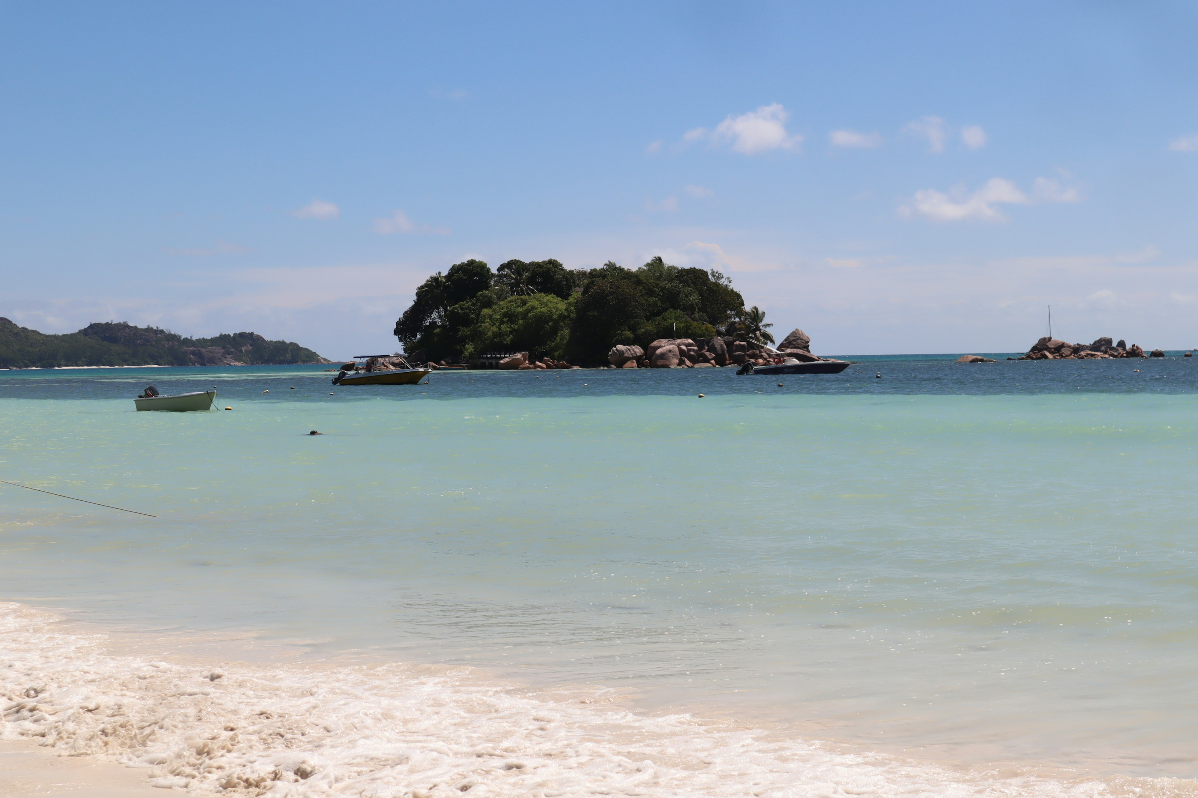 Paisaje de playa con mar azul y arena blanca pequeña isla de fondo con barcos flotando