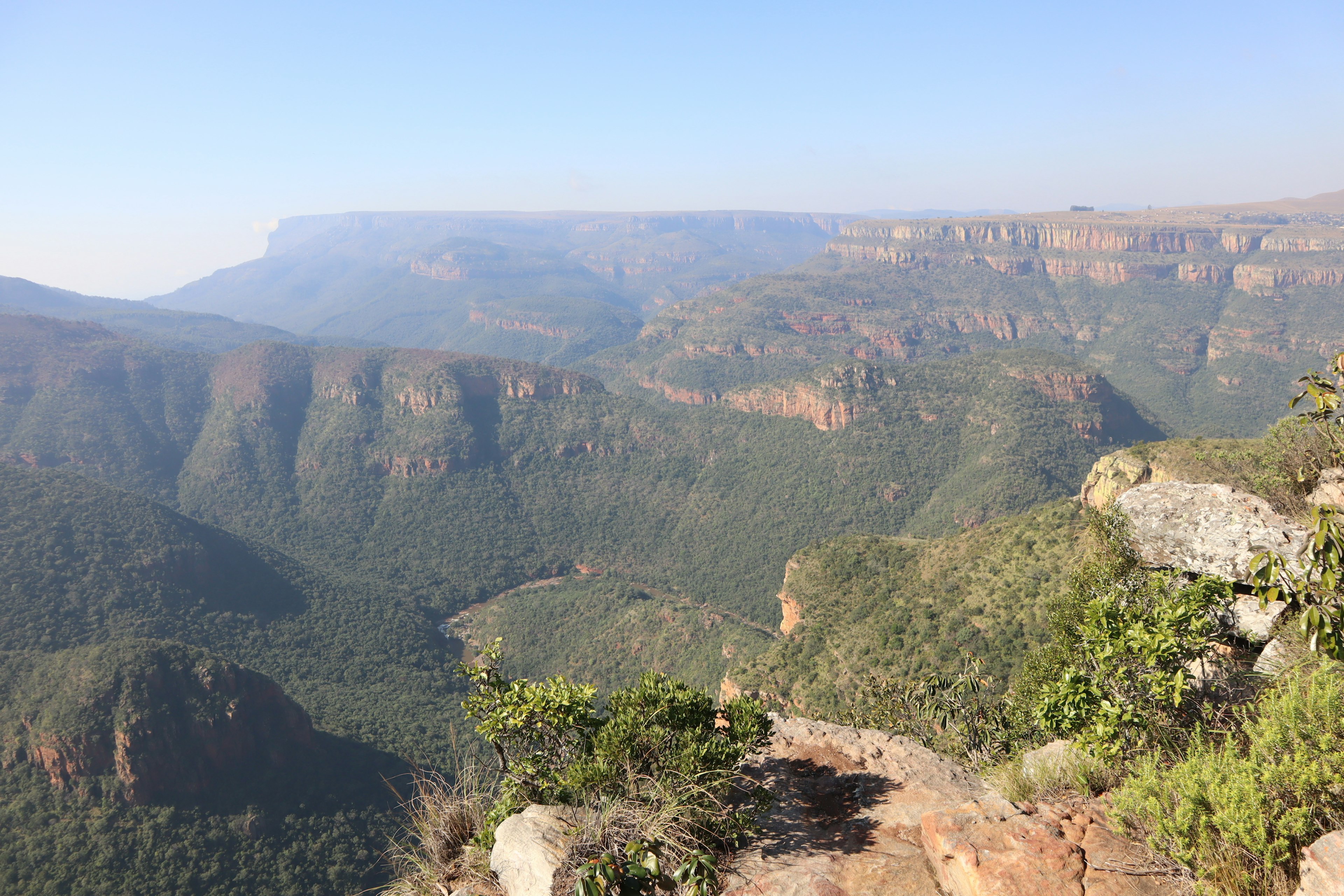 Expansive view of mountains and valleys under a blue sky with light mist