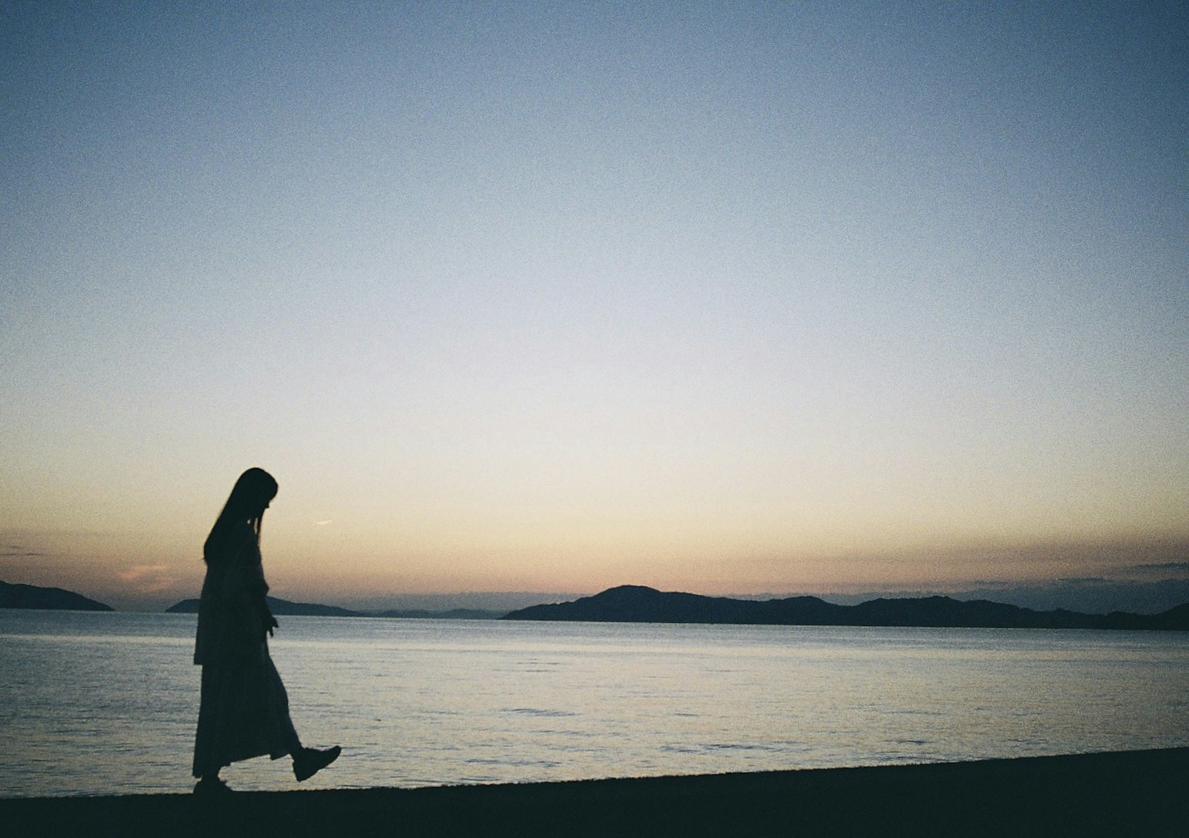 夕焼けの海辺を歩く女性のシルエット