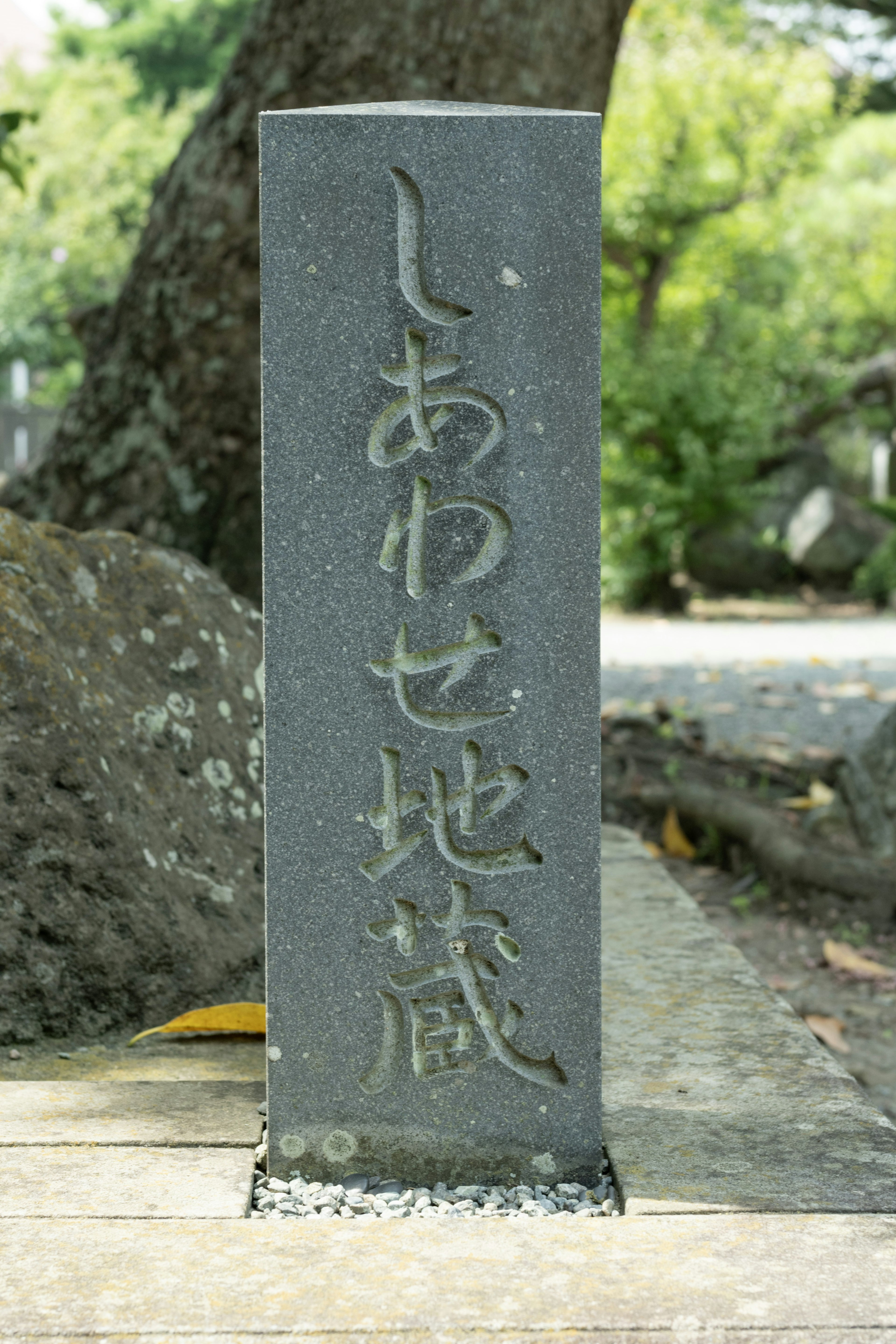 Un marqueur en pierre noire avec des inscriptions japonaises entouré de verdure