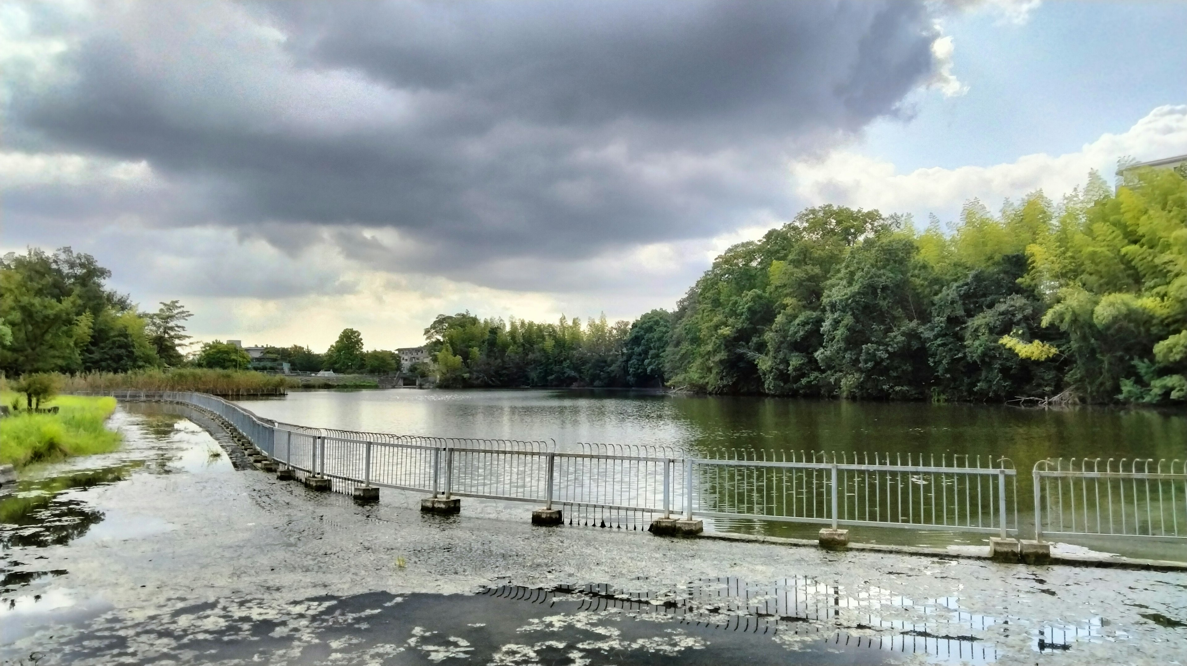 Pemandangan danau yang tenang dengan langit mendung dan jalan setapak