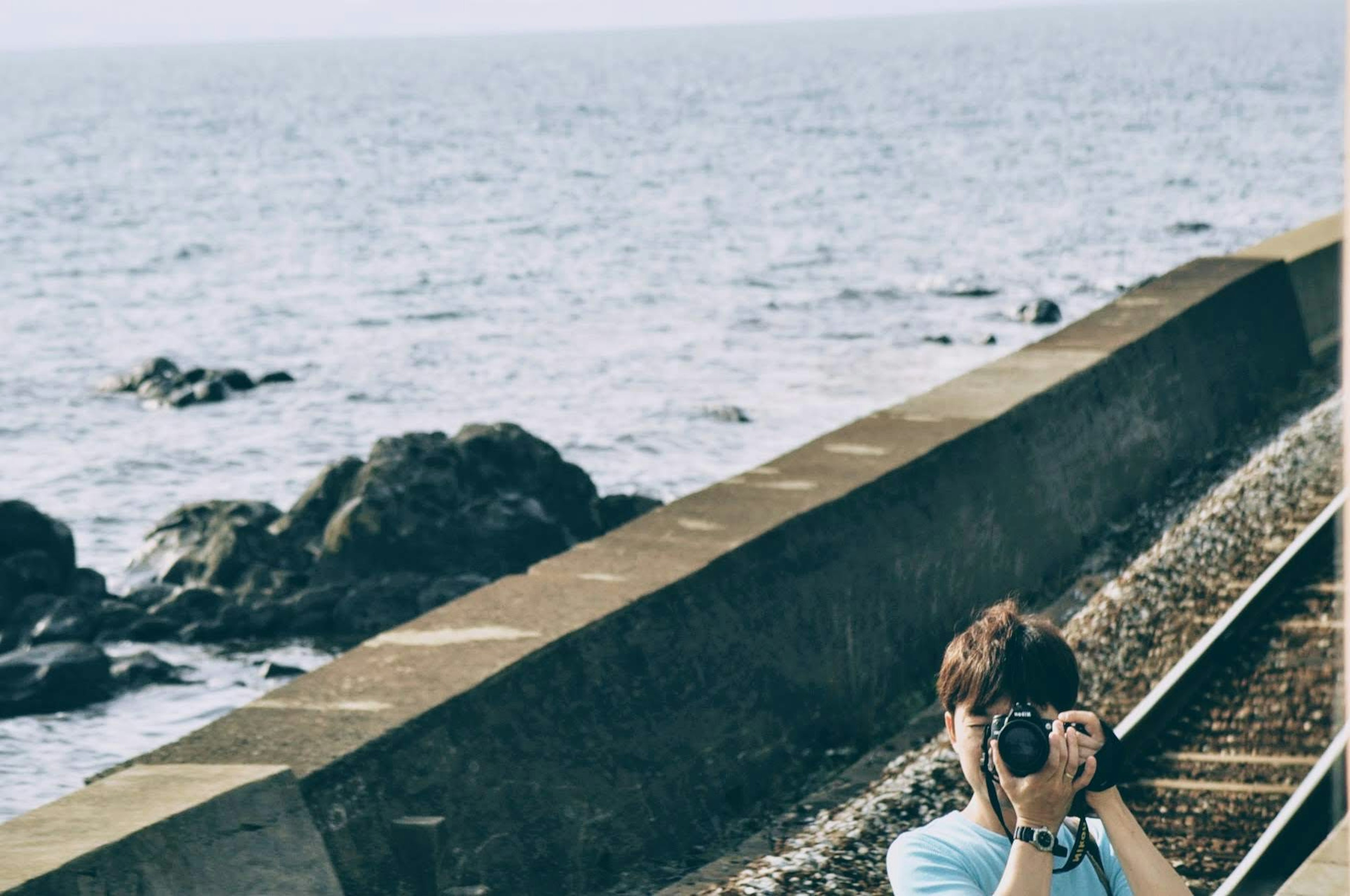 Young man holding a camera standing by the railway along the coast