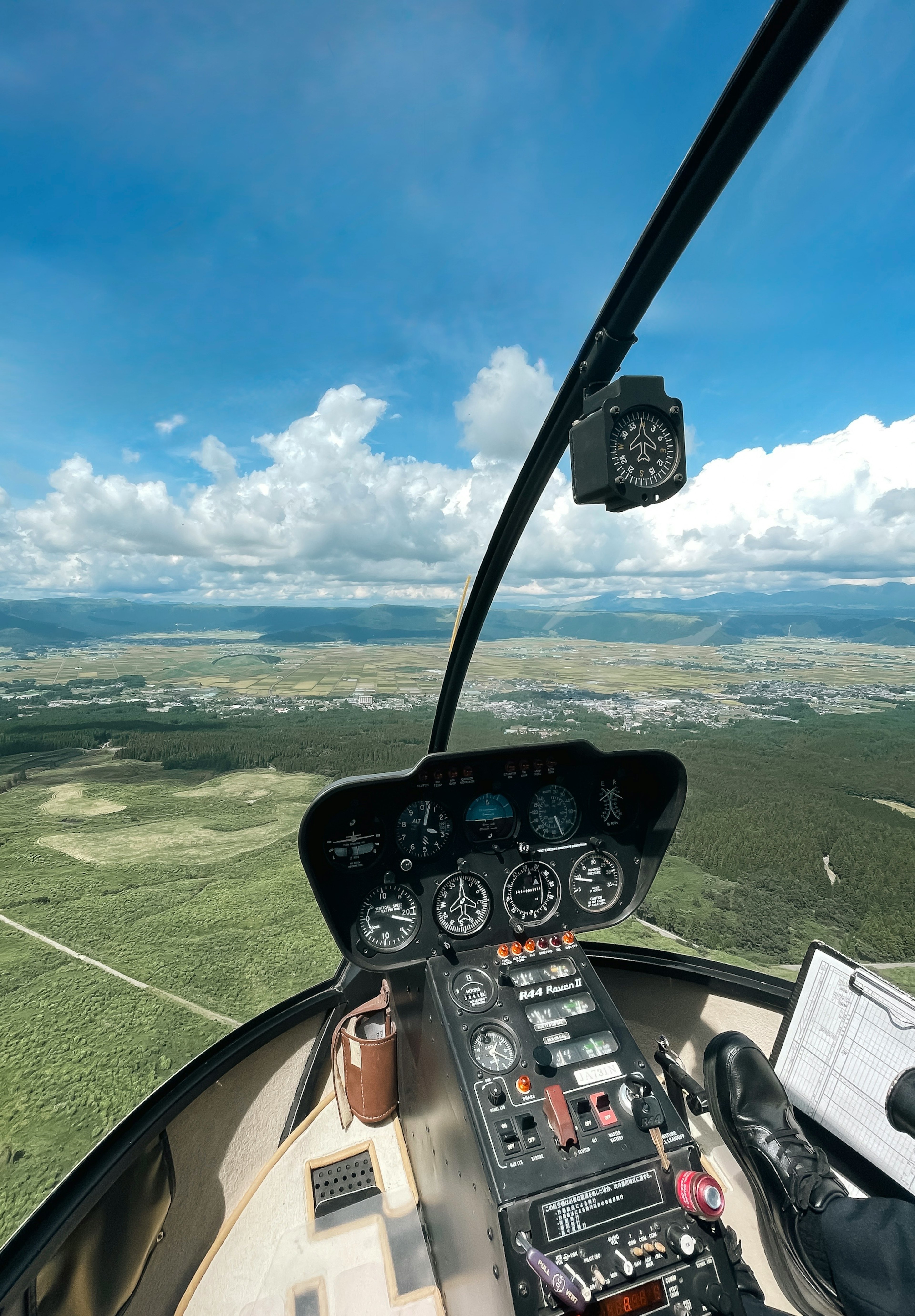 Vista desde la cabina de un helicóptero mostrando cielo azul nubes y paisaje verde