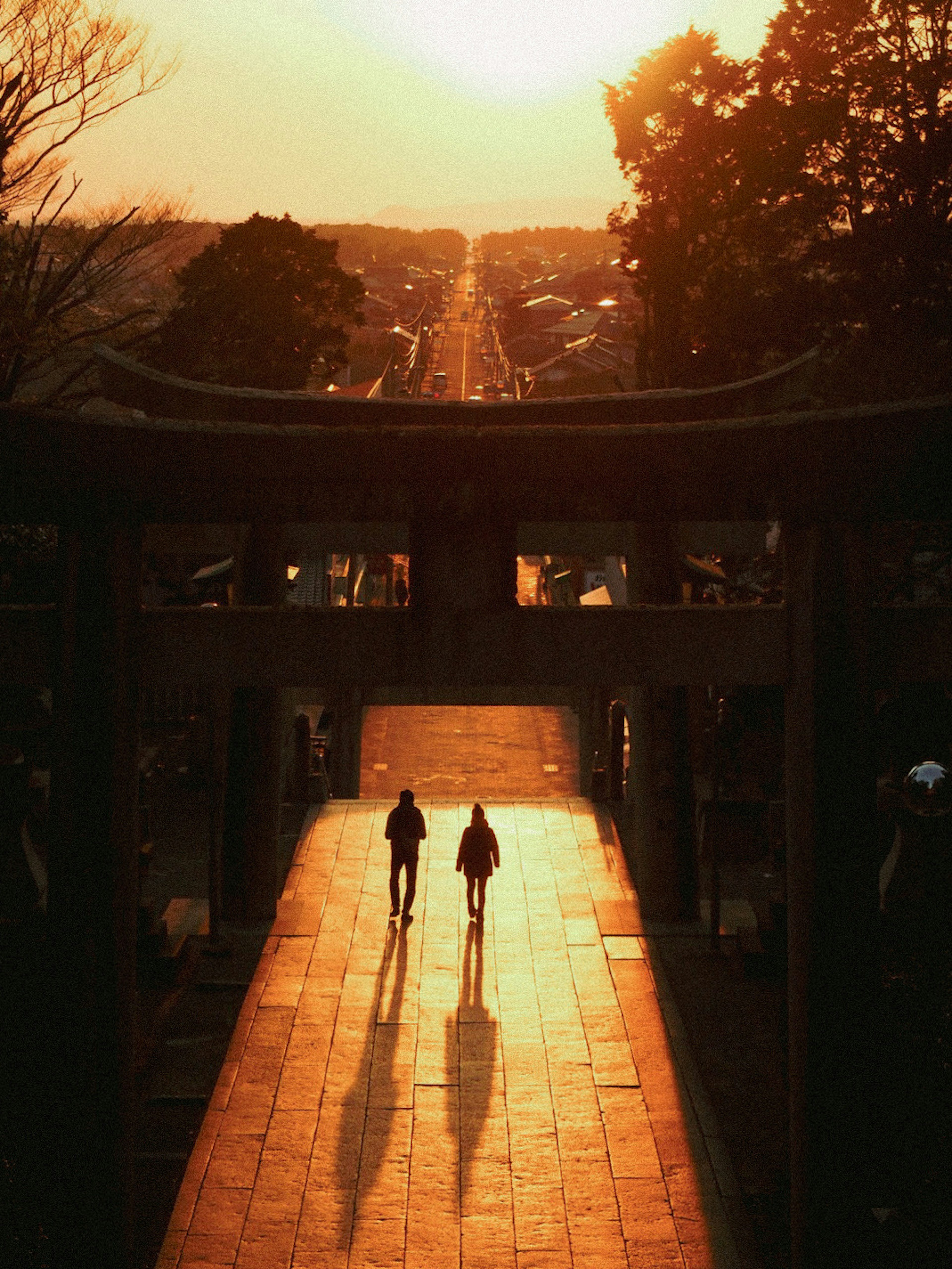 Silhouettes of two people walking through a shrine gate at sunset