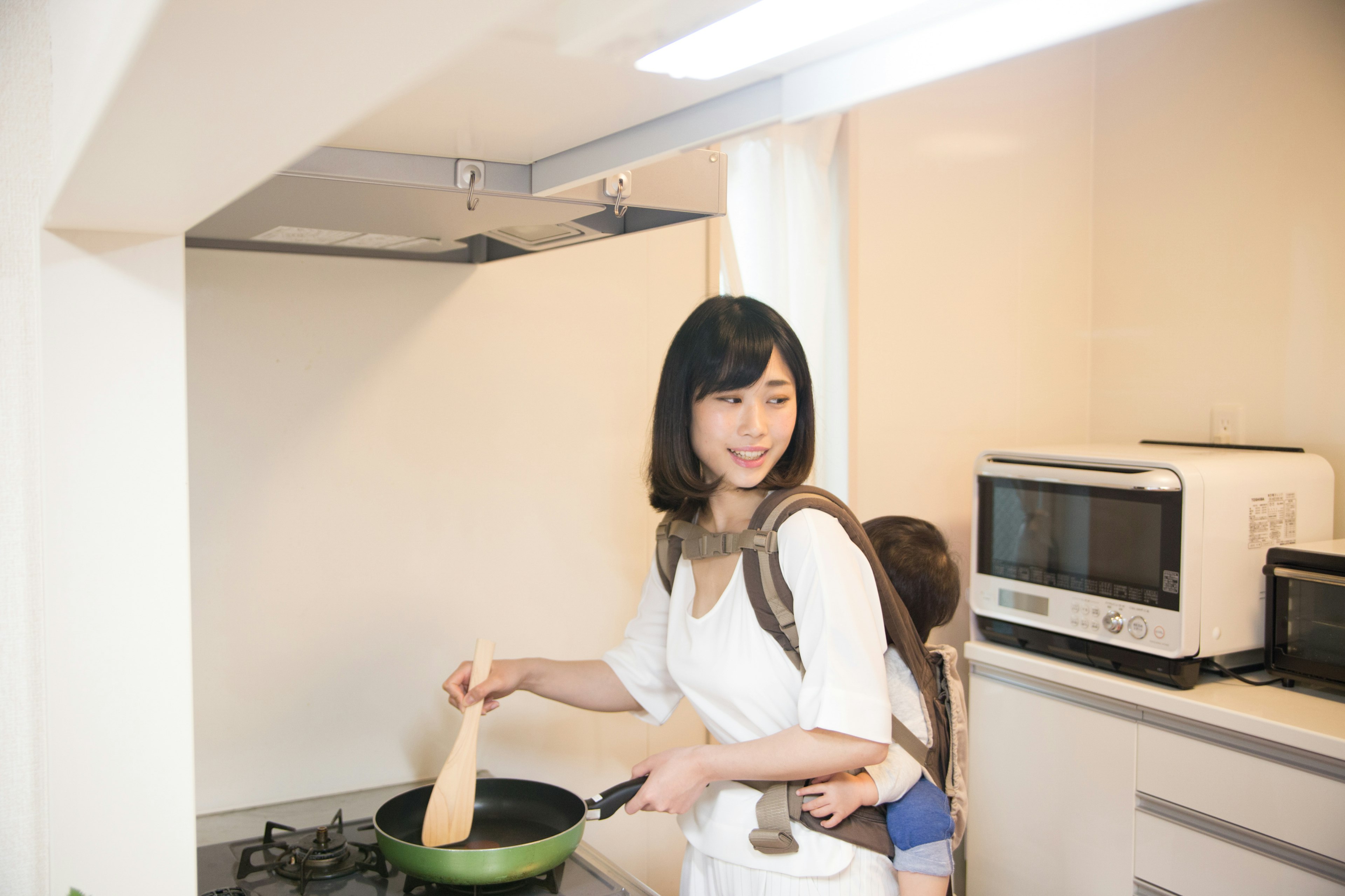 Femme cuisinant dans la cuisine tout en portant un enfant sur le dos