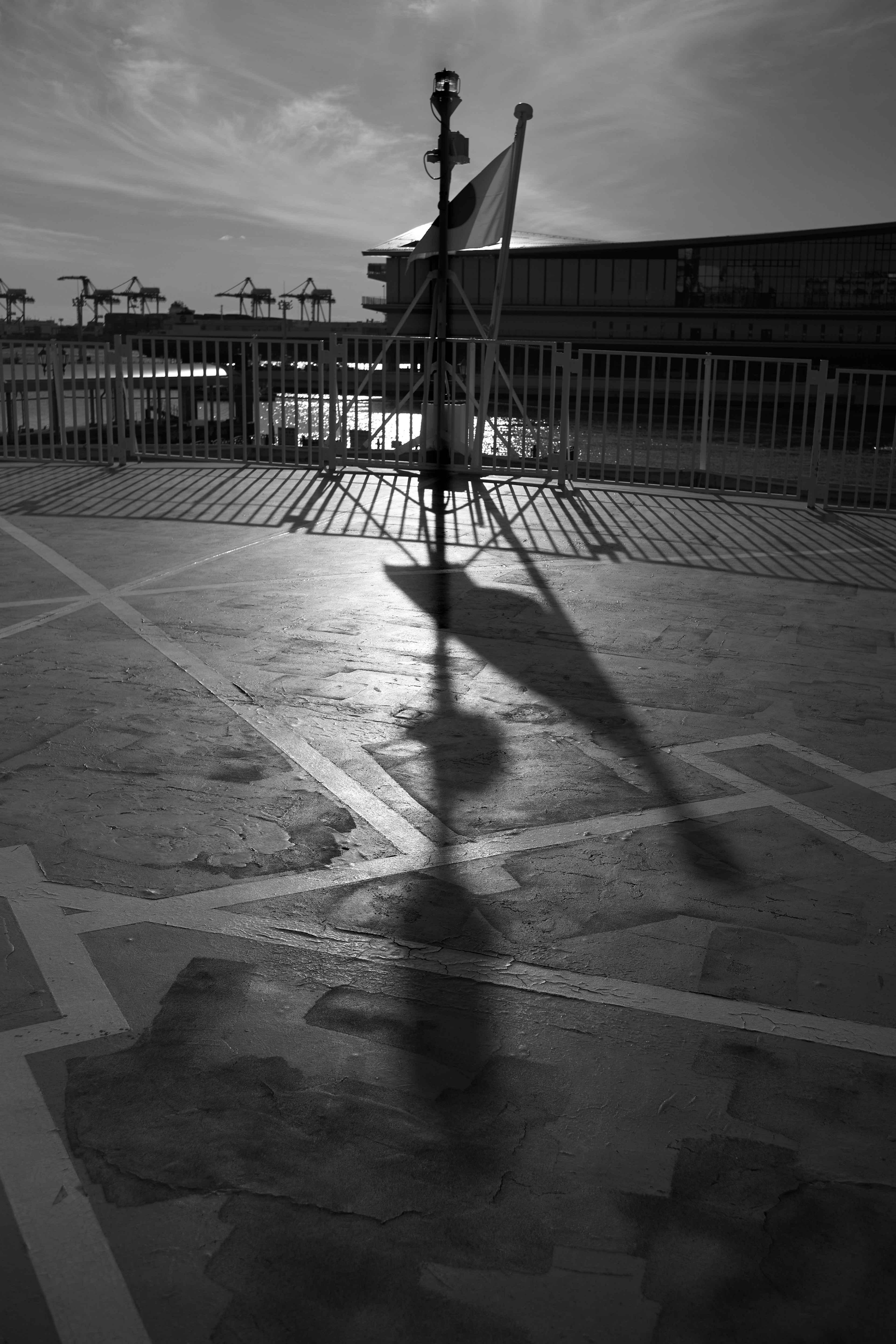 Black and white photo of a flagpole casting a long shadow on the ground