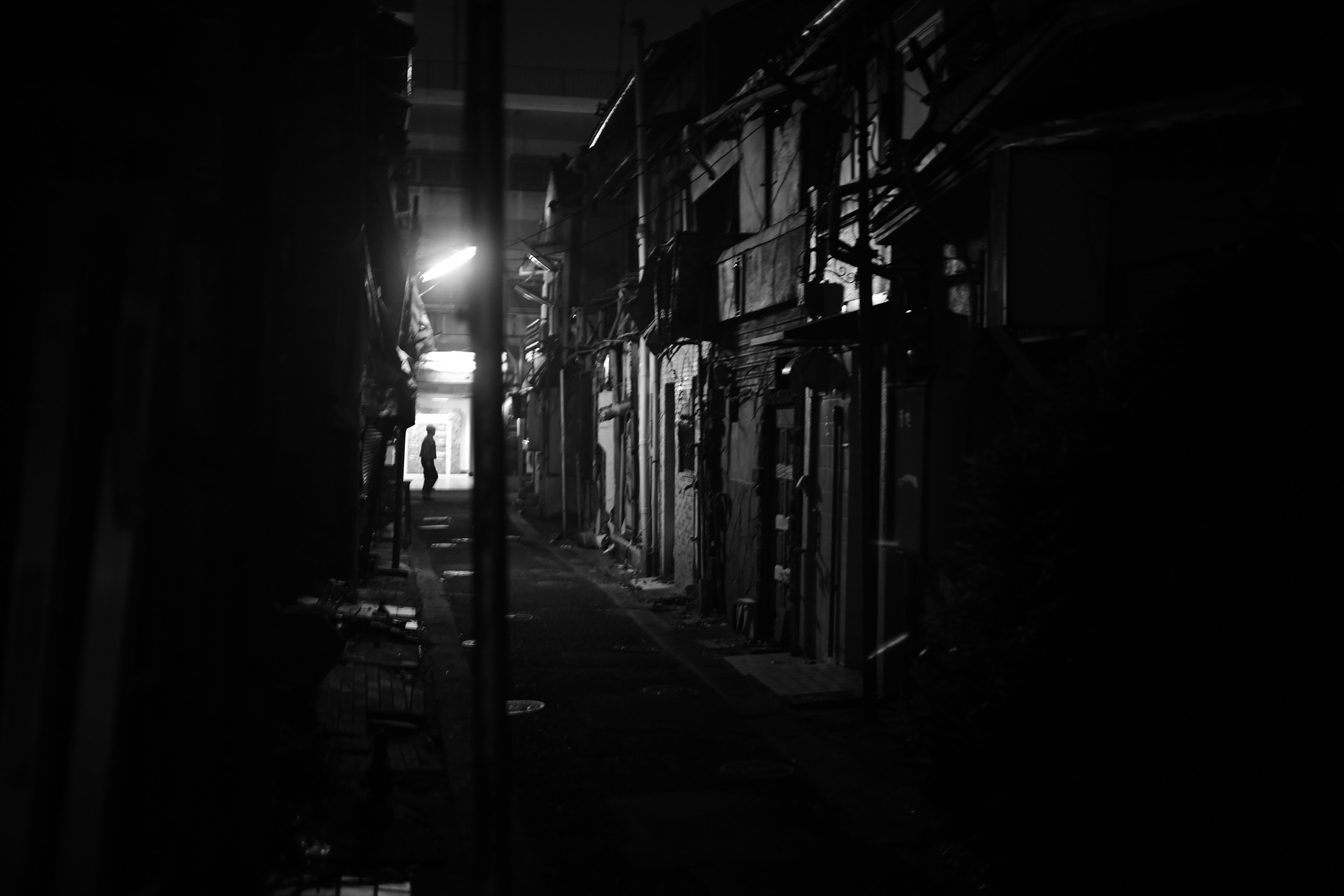 Photo en noir et blanc d'une ruelle étroite avec des bâtiments et un lampadaire