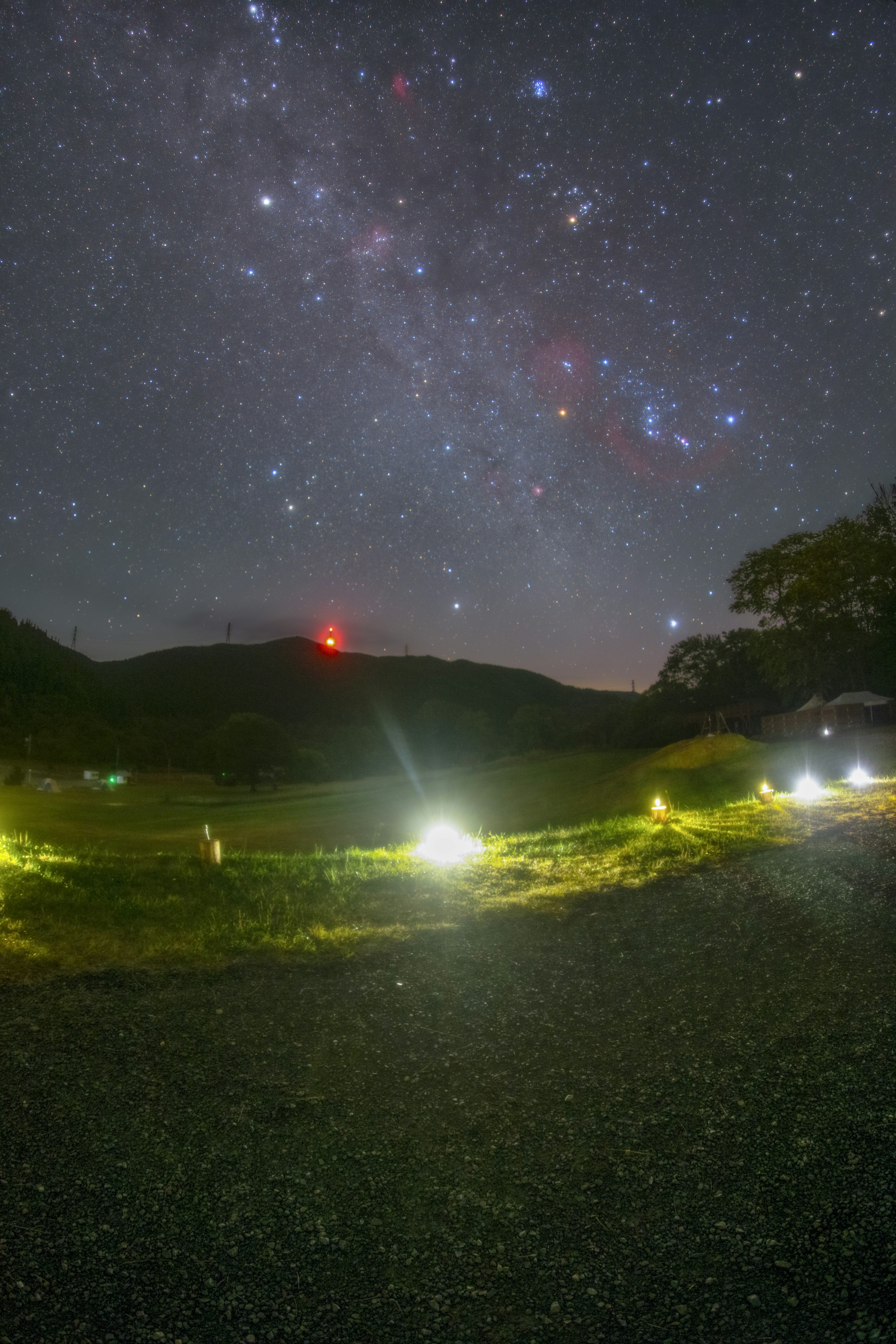 星空と山の風景に照らされた草原の夜景