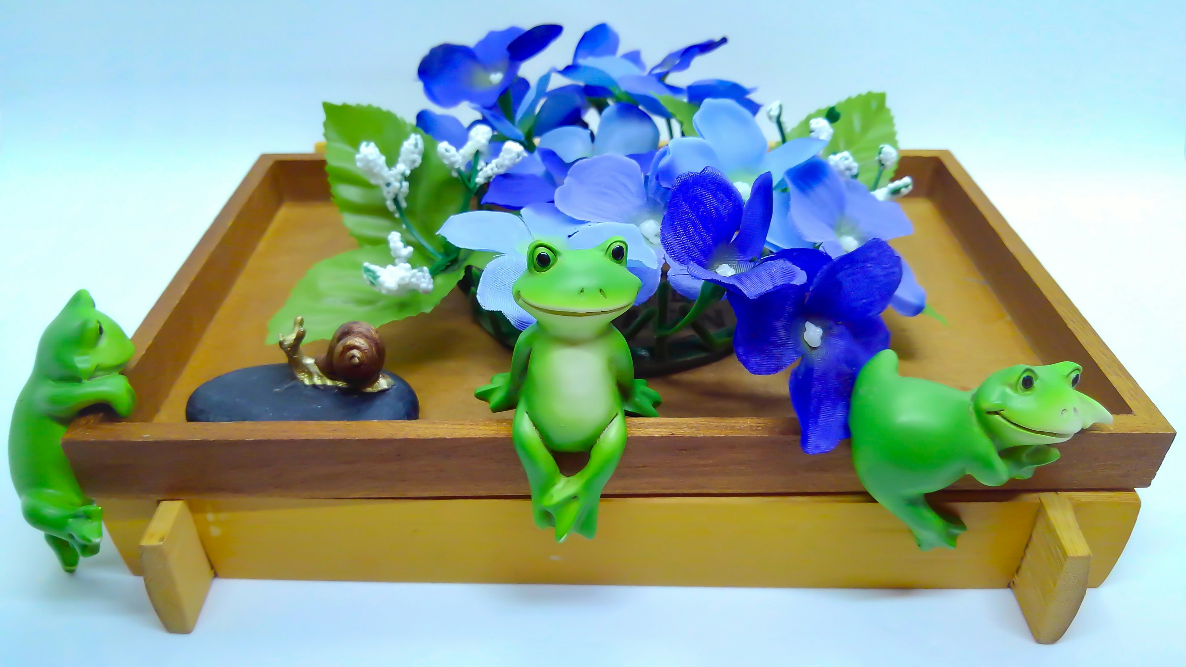 Green frog figurines arranged around a bouquet of blue flowers