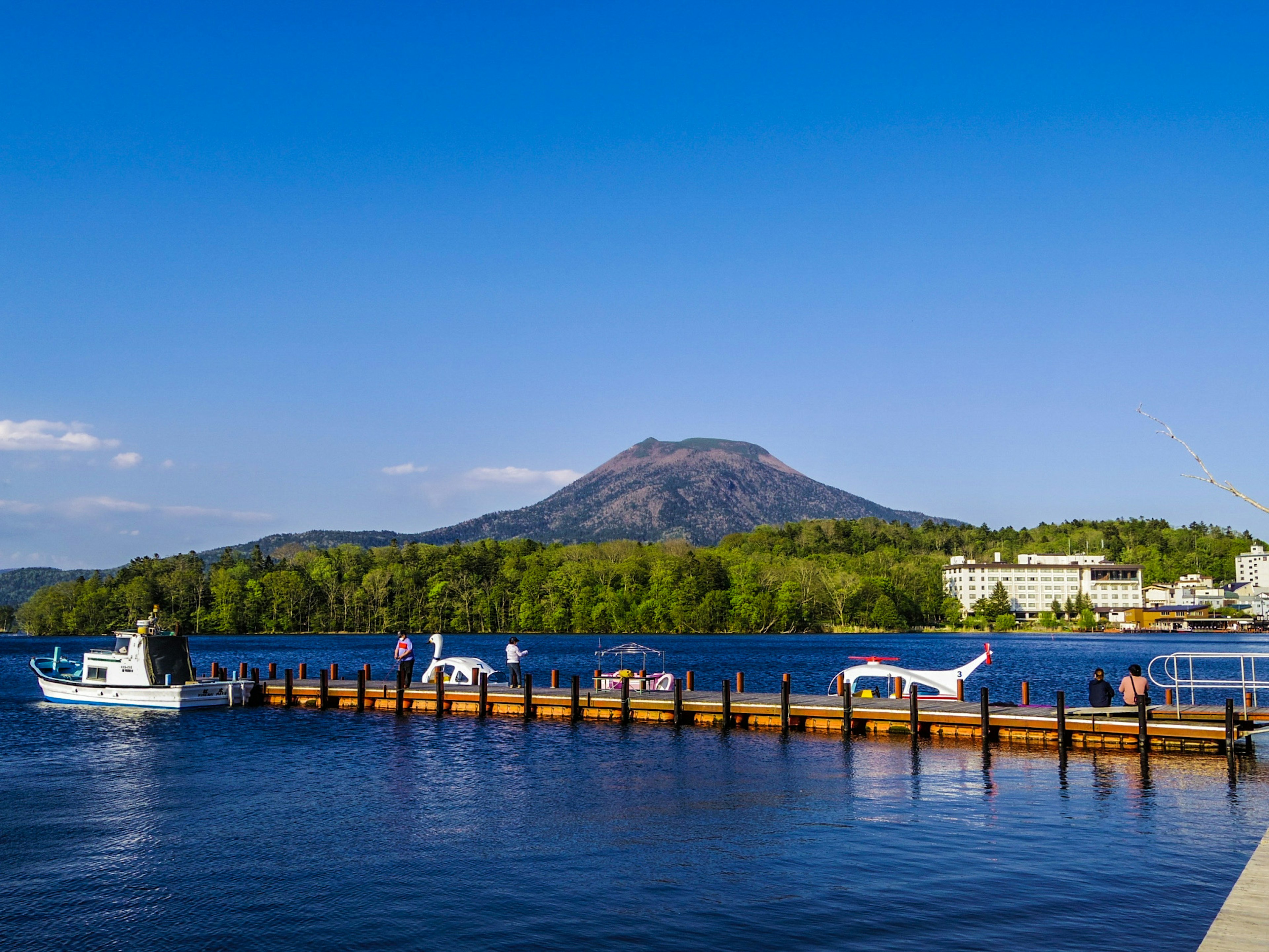 ทิวทัศน์ที่สวยงามของทะเลสาบพร้อมท่าเรือและภูเขาในพื้นหลังเรือจอด