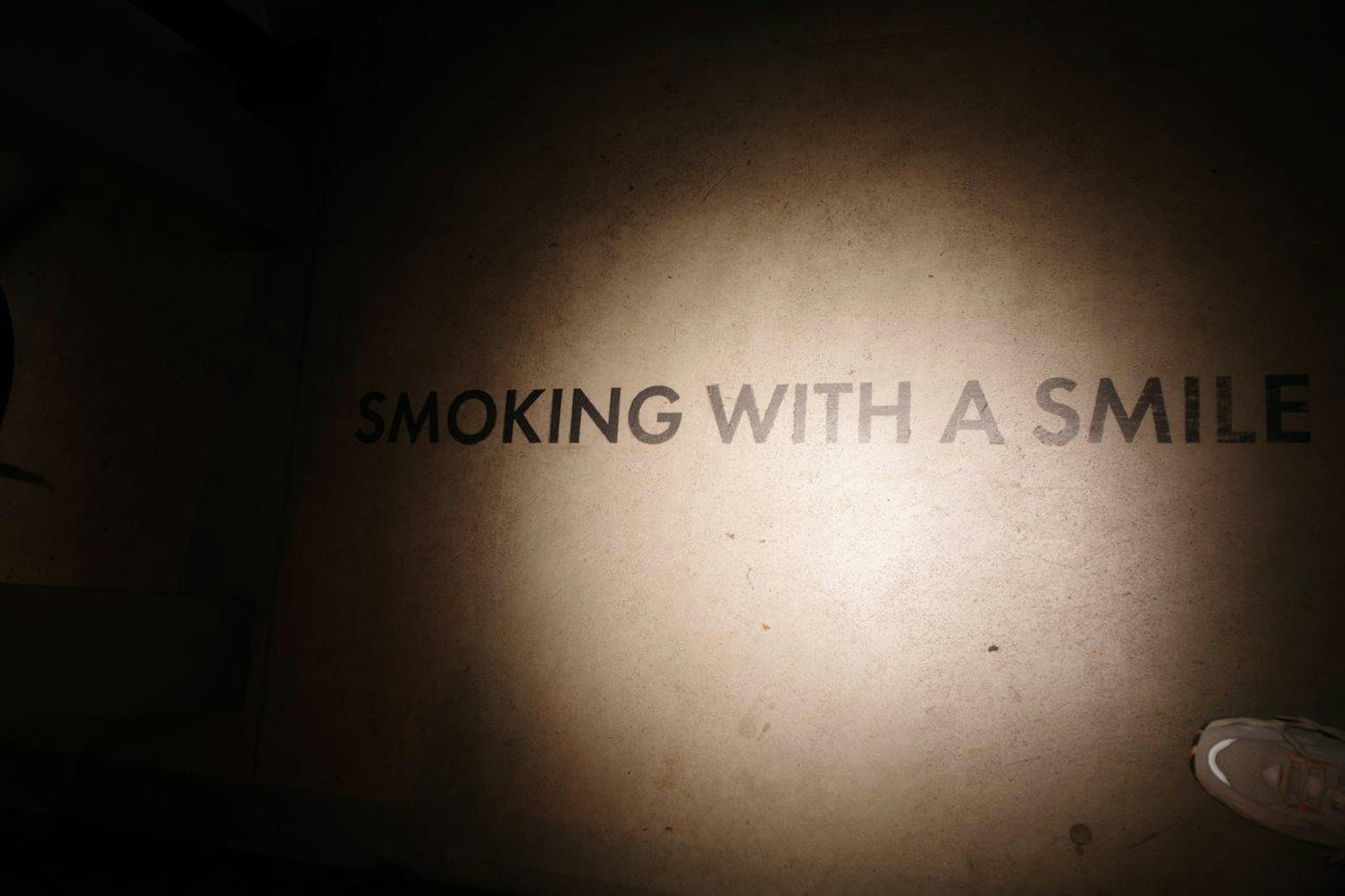 ข้อความสีขาว "SMOKING WITH A SMILE" ส่องสว่างบนพื้นหลังมืด