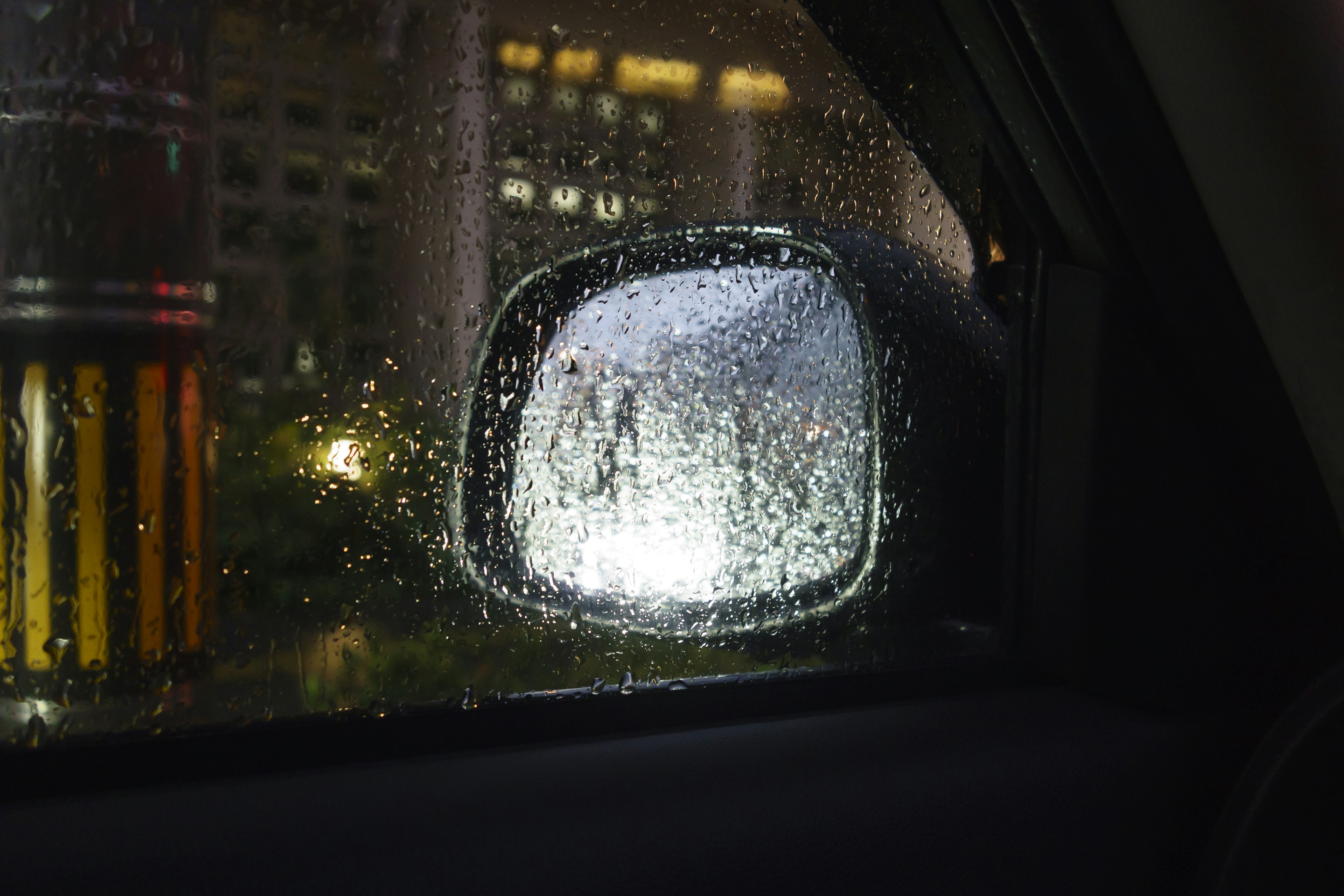 Rain-soaked side mirror viewed from a car window at night