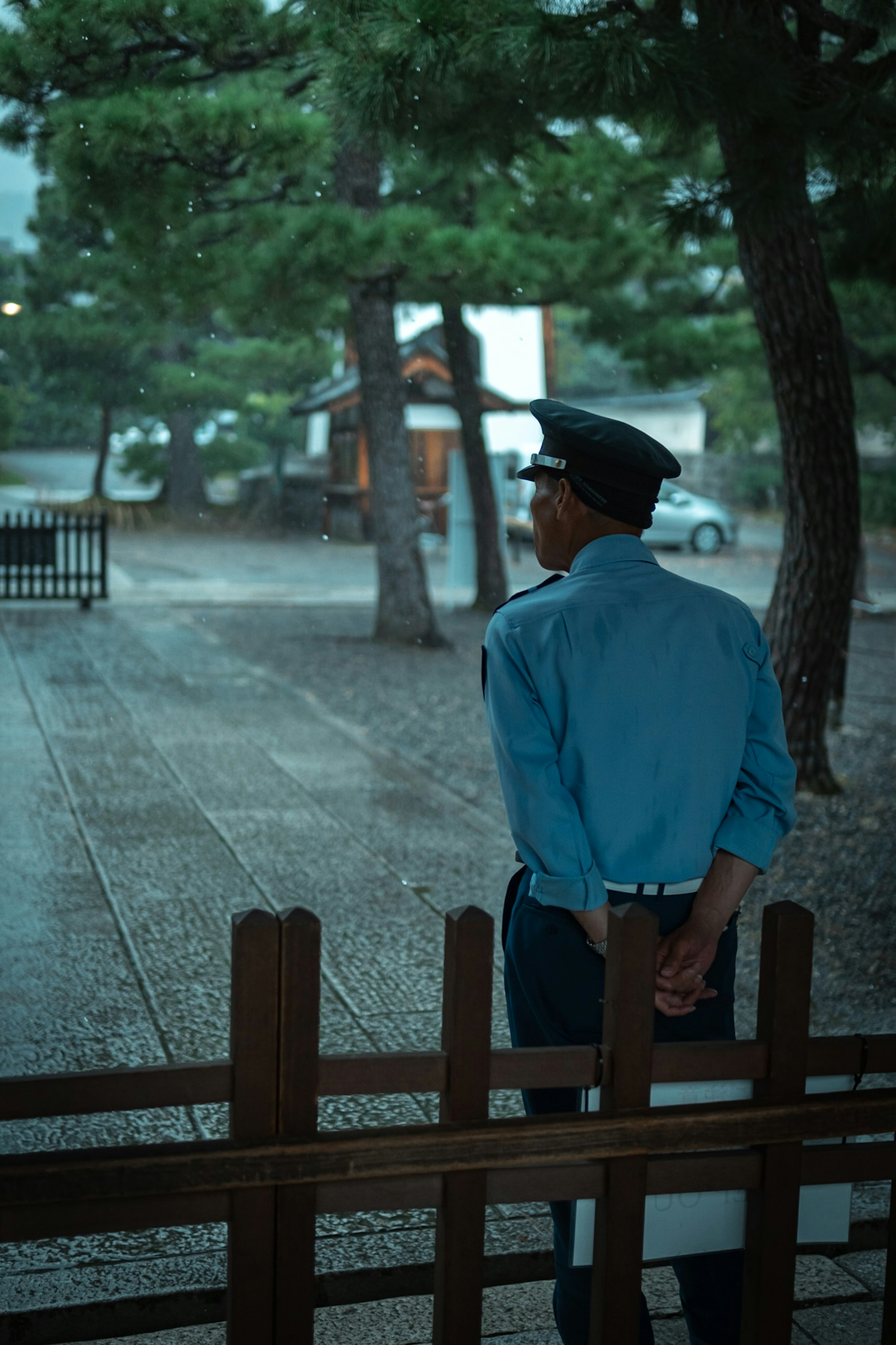 青い制服を着た警官が背を向けて立っている雨の中の風景