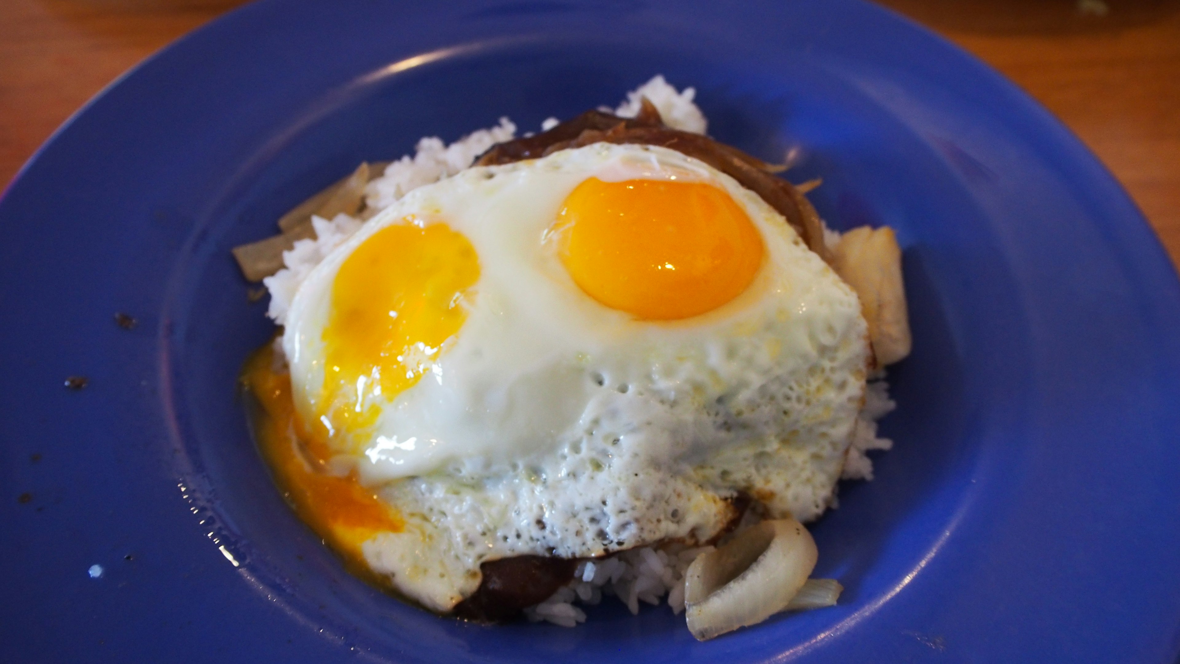 Deux œufs au plat sur un lit de riz servi dans une assiette bleue