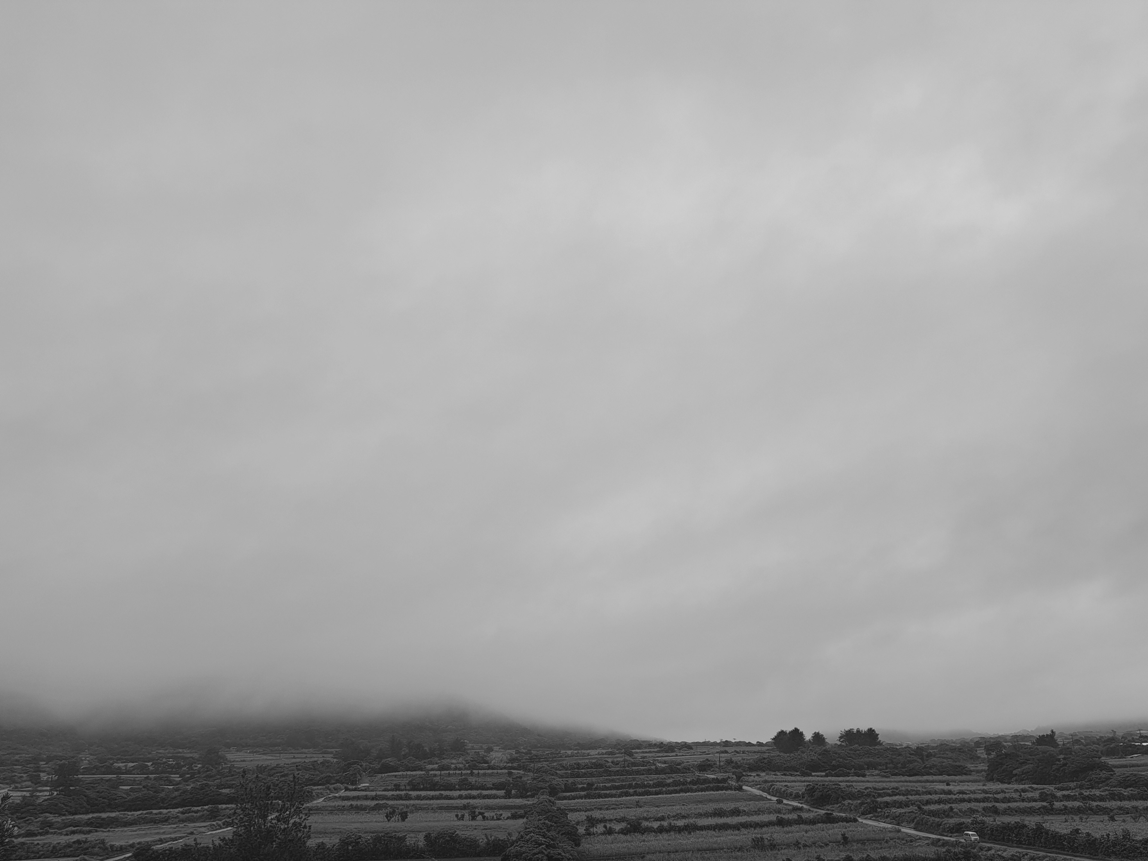 Landschaft mit Landwirtschaft und Bergen unter einem bewölkten Himmel