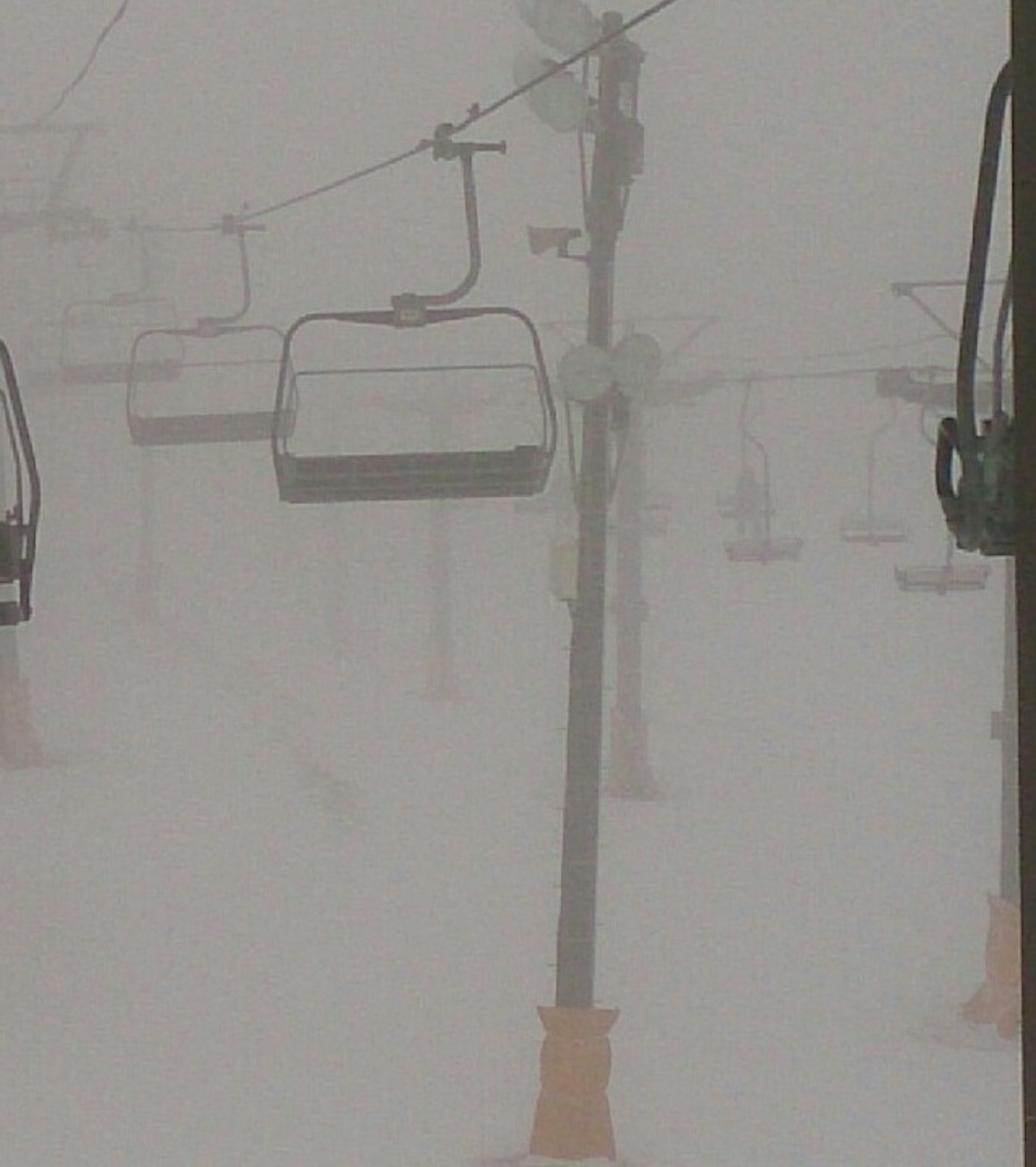 Snow-covered ski lift scene with poor visibility in winter weather