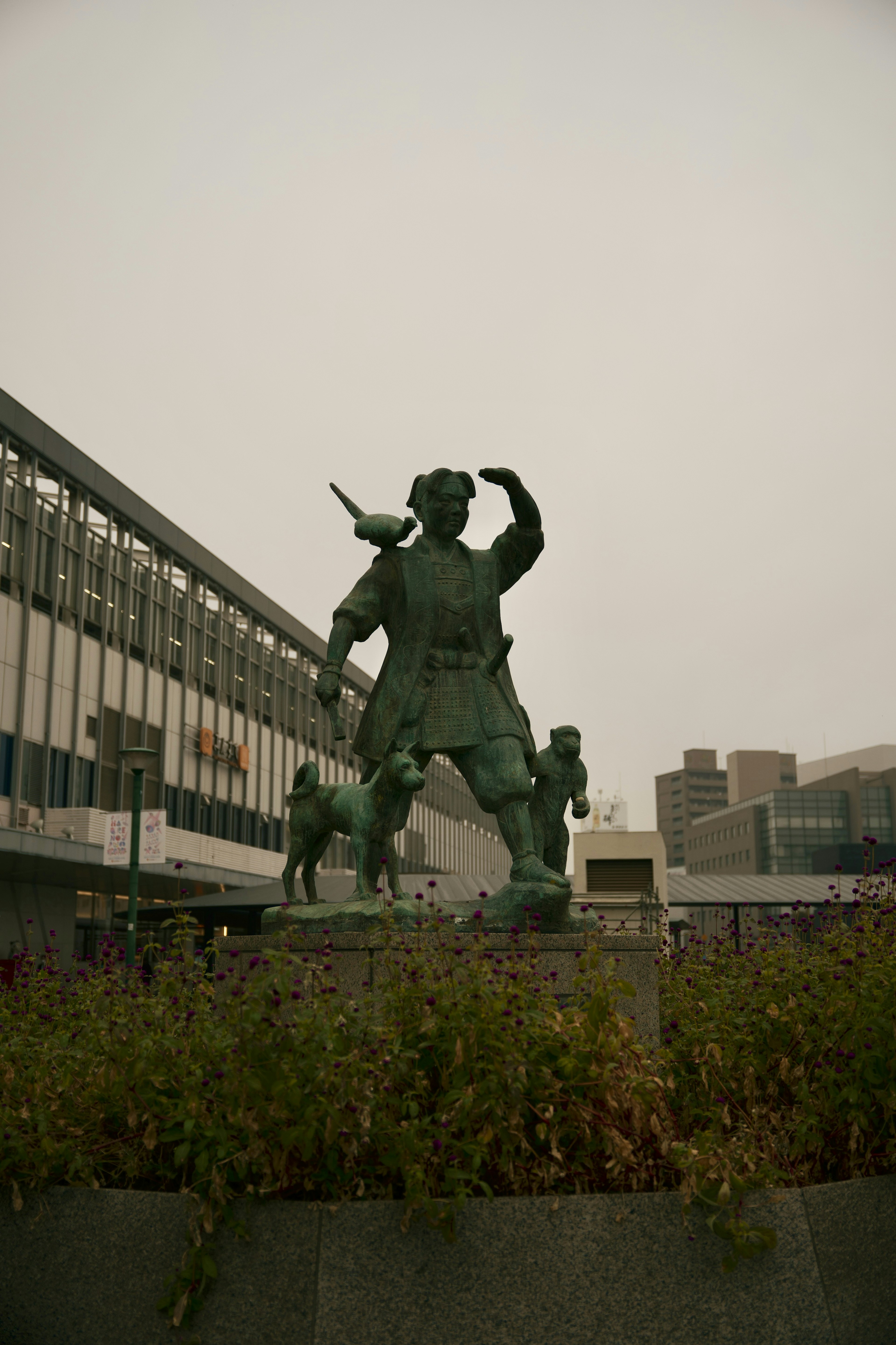 Statue en bronze se tenant devant une gare entourée de verdure