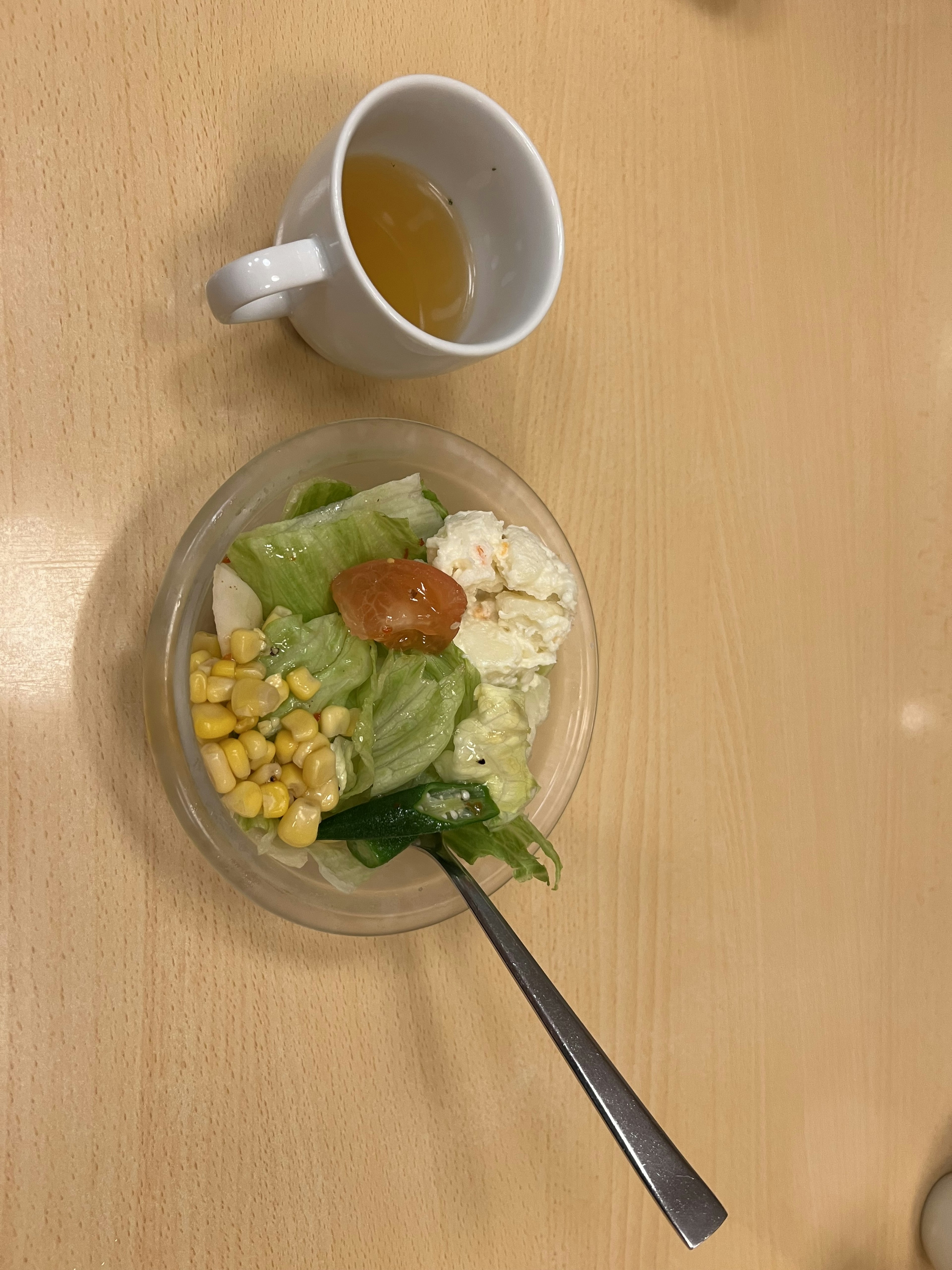 Semangkuk salad dengan selada, jagung, dan tomat di samping secangkir teh herbal