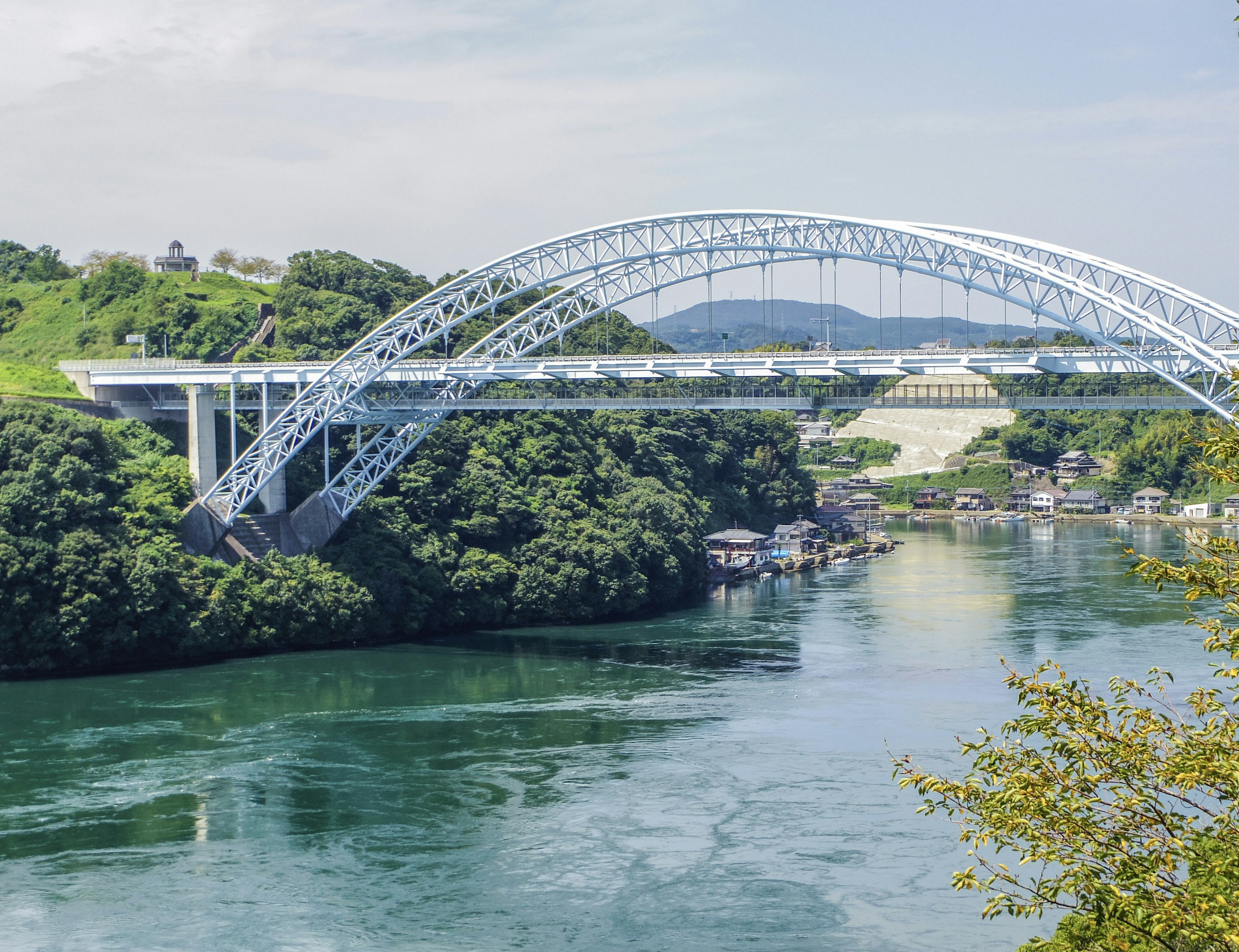 Un pont en arc bleu surplombe une rivière verte entourée de végétation luxuriante