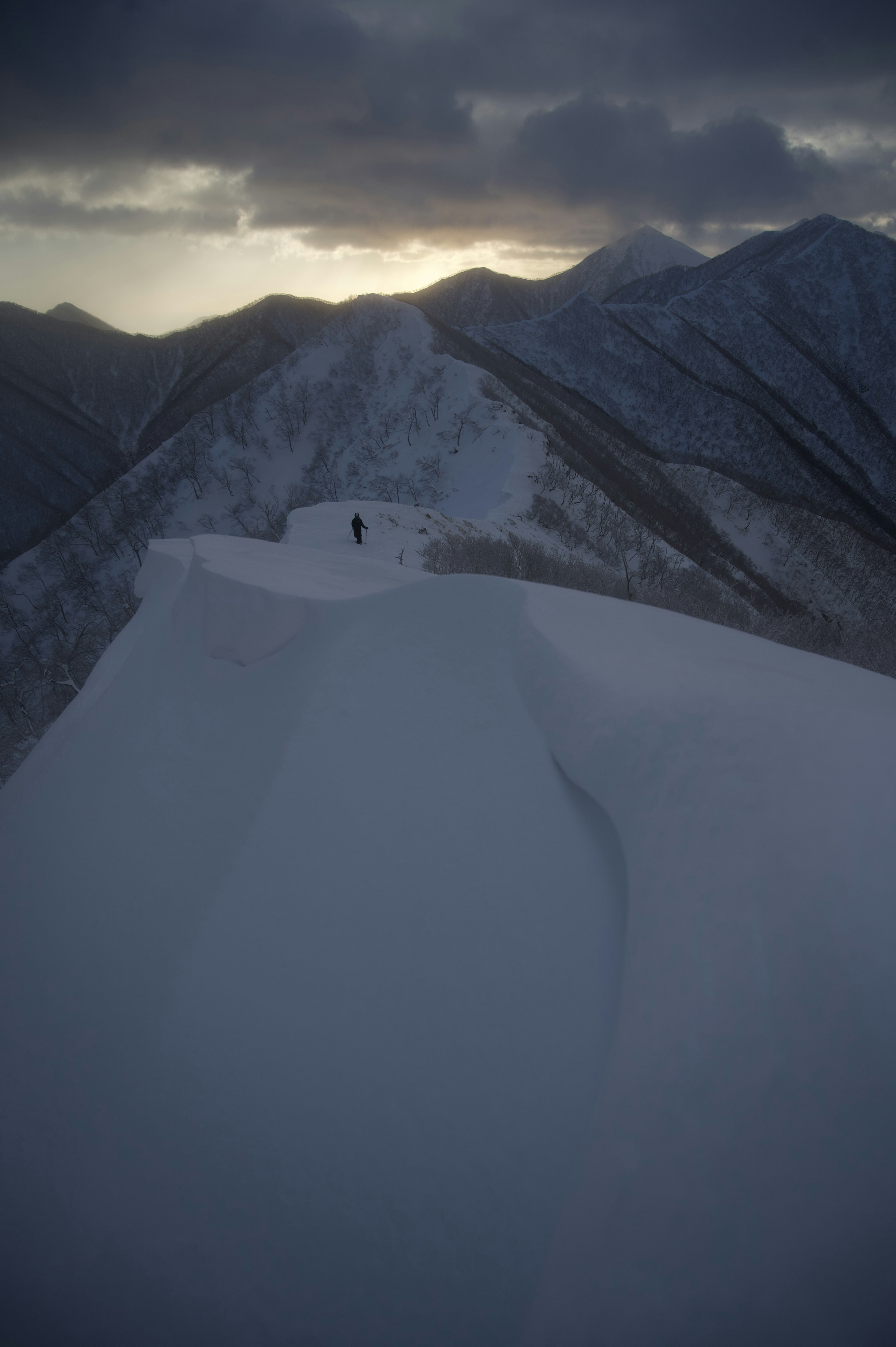 Silhouette di un escursionista che cammina lungo una cresta montuosa coperta di neve