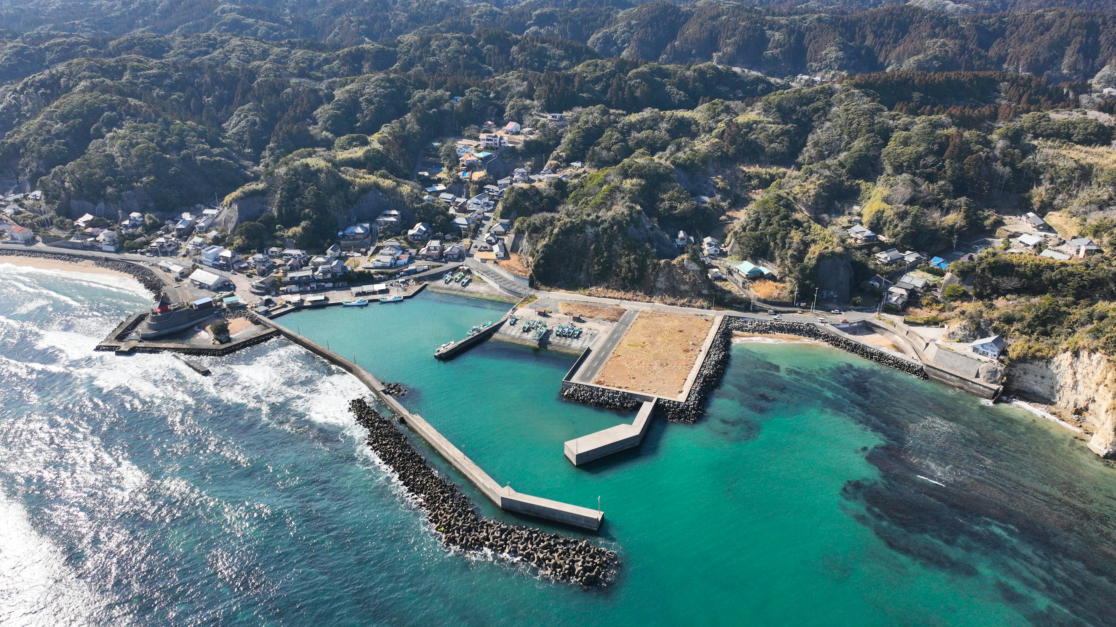 Vista aérea de un pueblo costero con un puerto rodeado de colinas verdes y mar azul