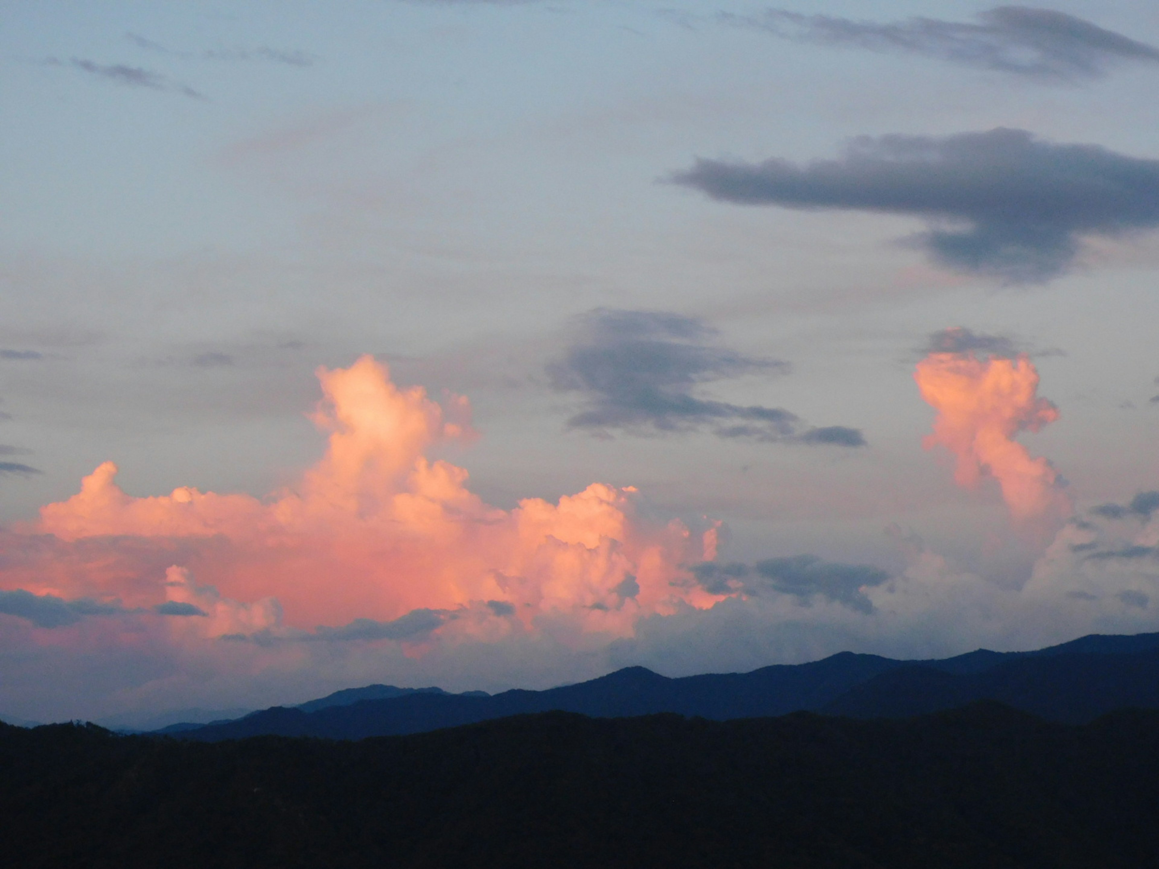 Pink clouds against a blue sky with silhouettes of mountains