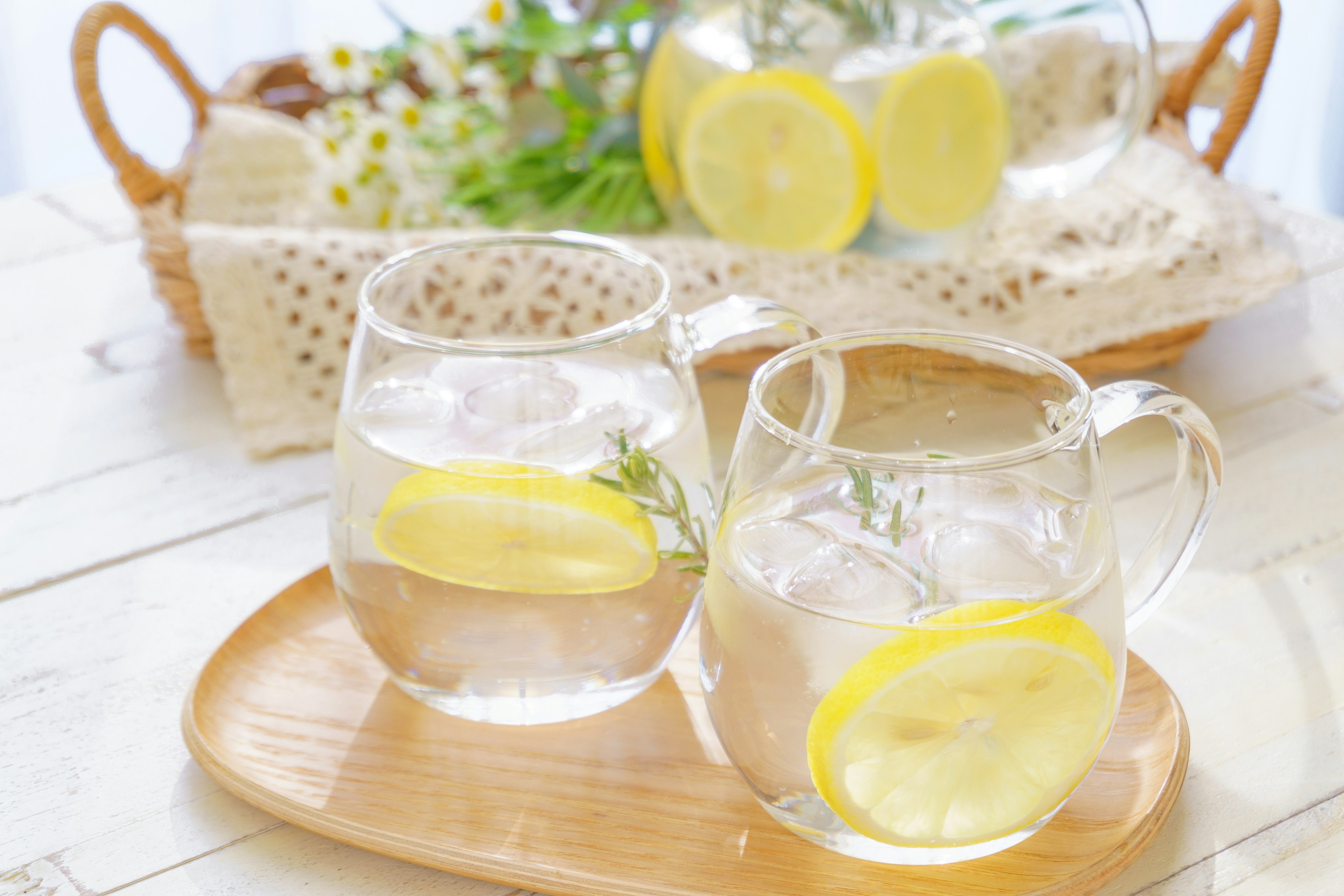 Vasos transparentes llenos de agua y rodajas de limón en una bandeja de madera