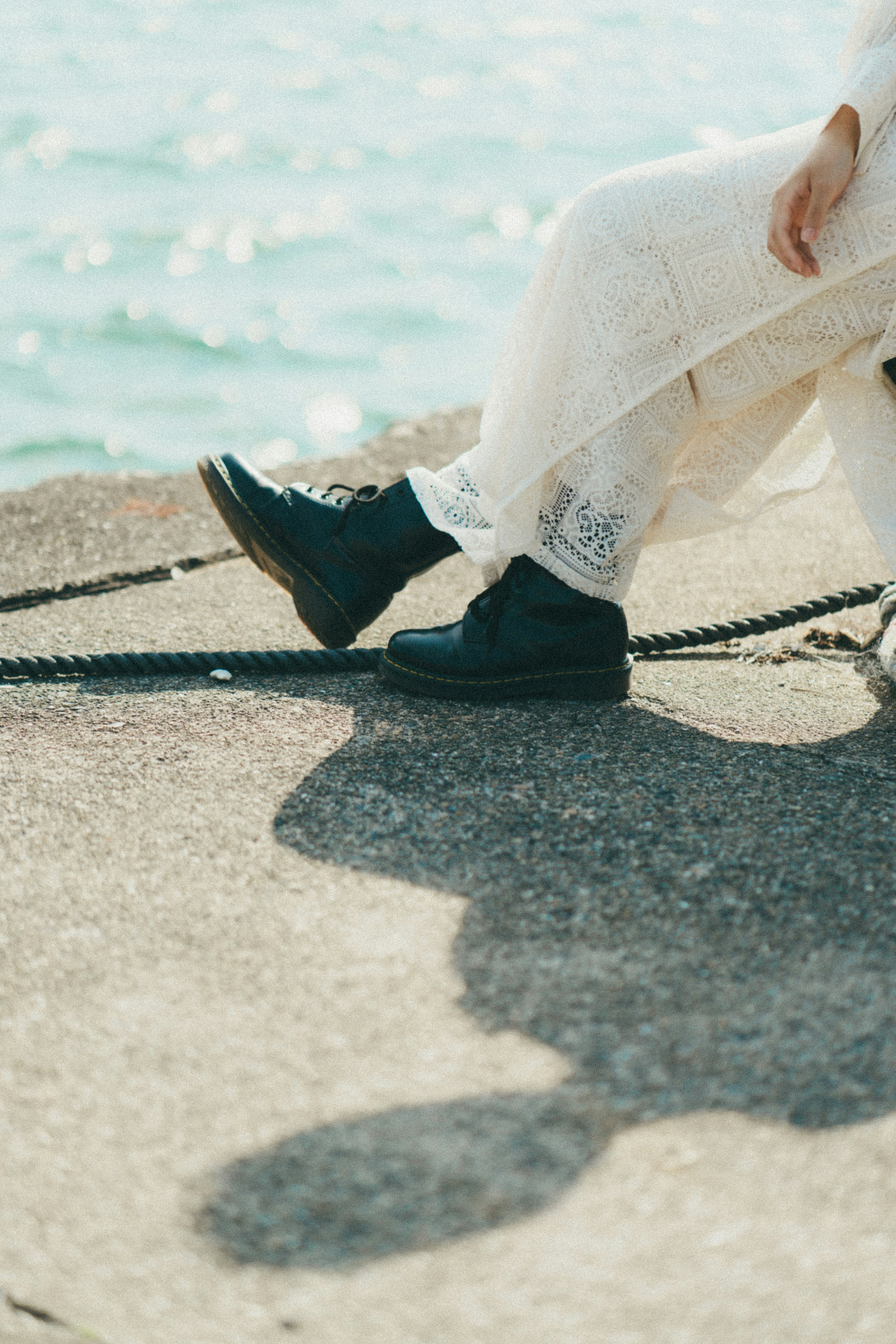 Close-up of black boots on a concrete surface by the sea with a shadow