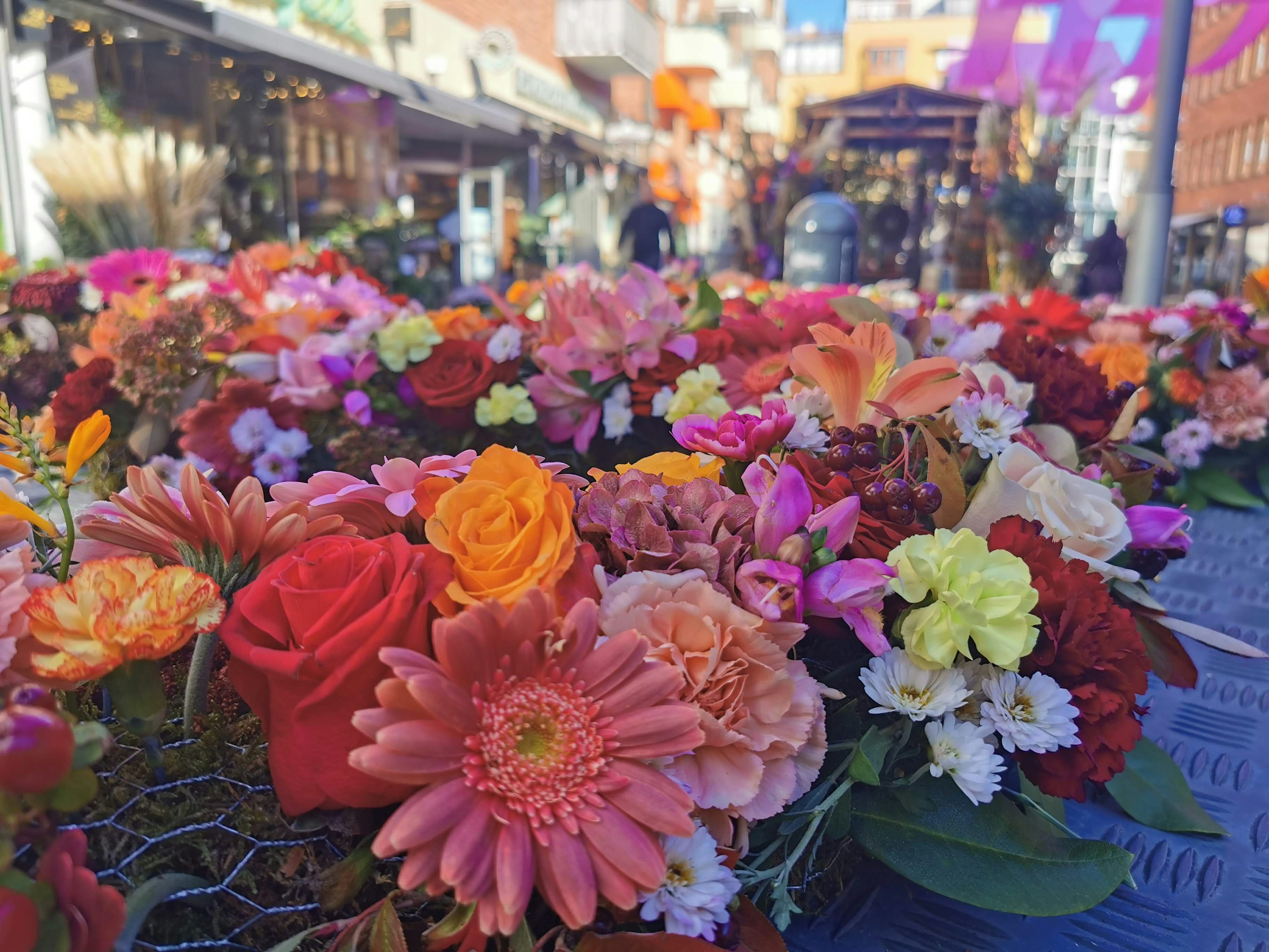 Una colorida variedad de flores en una escena de mercado Primer plano de flores con personas al fondo